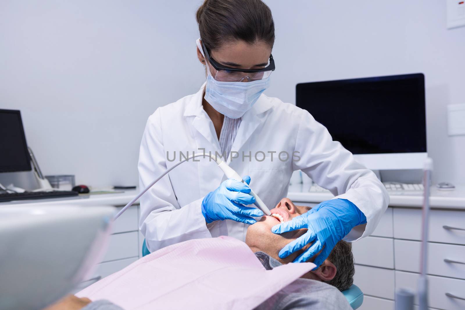 Dentist holding equipment while giving treatment to man by Wavebreakmedia