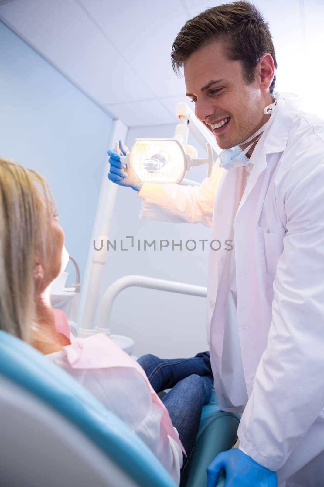 Dentist adjusting lamp while looking at patient in clinic by Wavebreakmedia