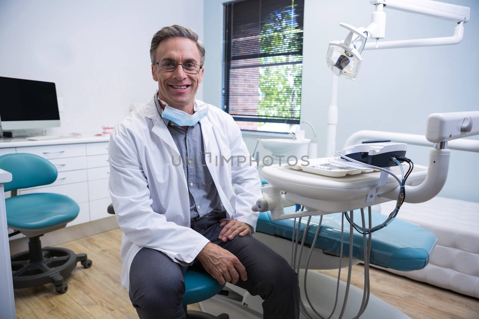 Portrait of smiling dentist sitting on chair by Wavebreakmedia