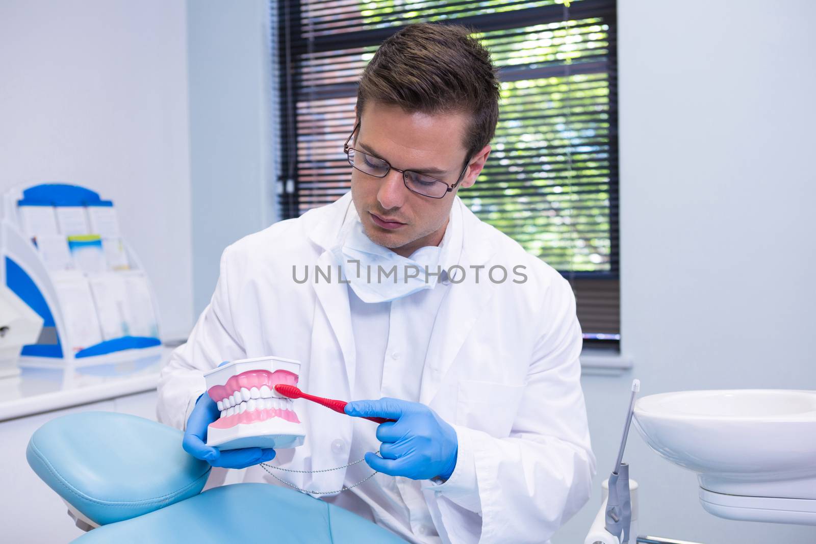 Dentist brushing dental mold while sitting at clinic