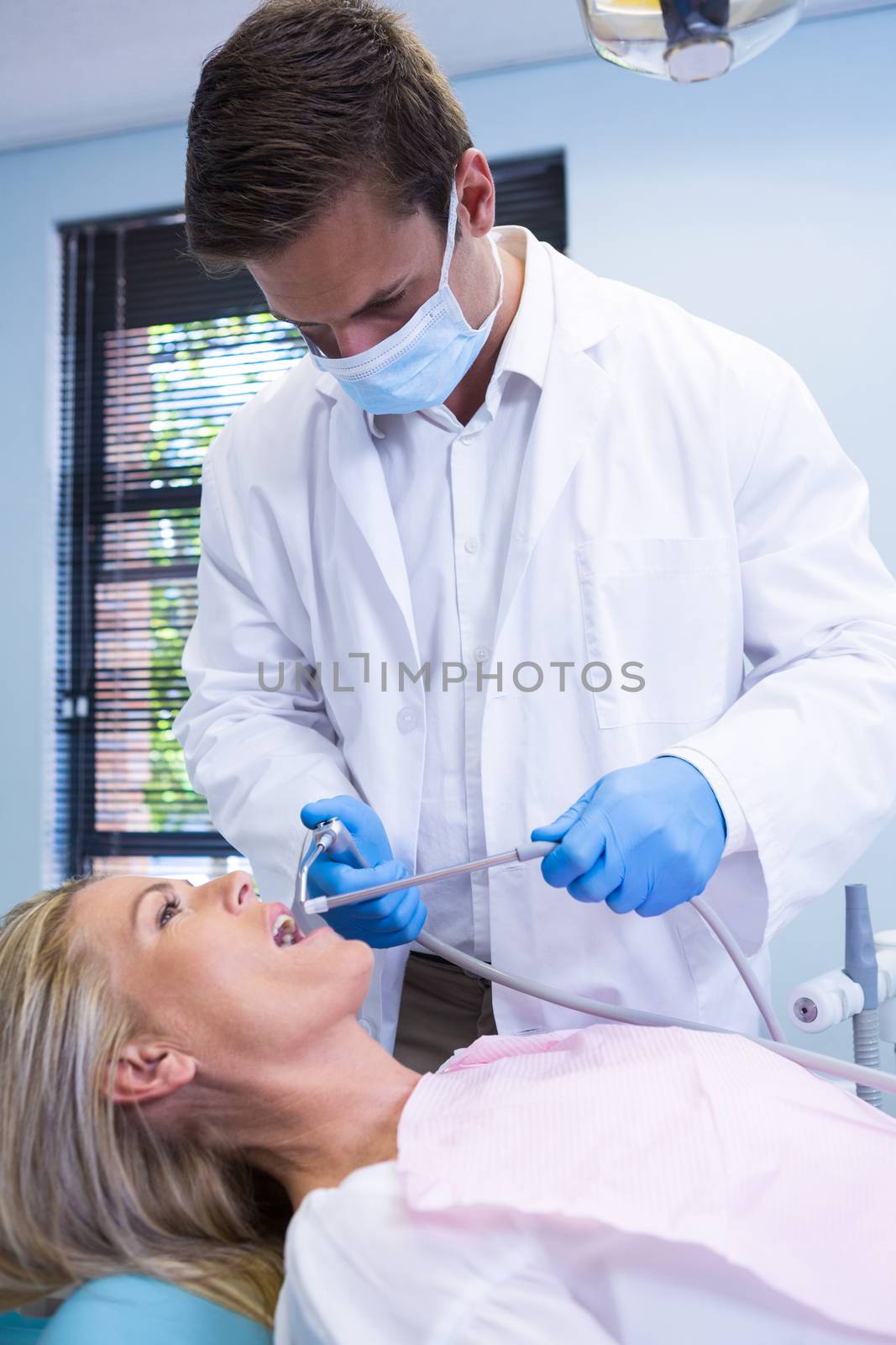 Dentist cleaning woman teeth while standing against wall by Wavebreakmedia