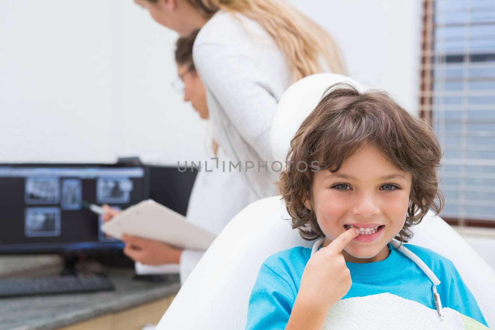Little boy smiling at camera with mother and dentist in background at the dental clinic