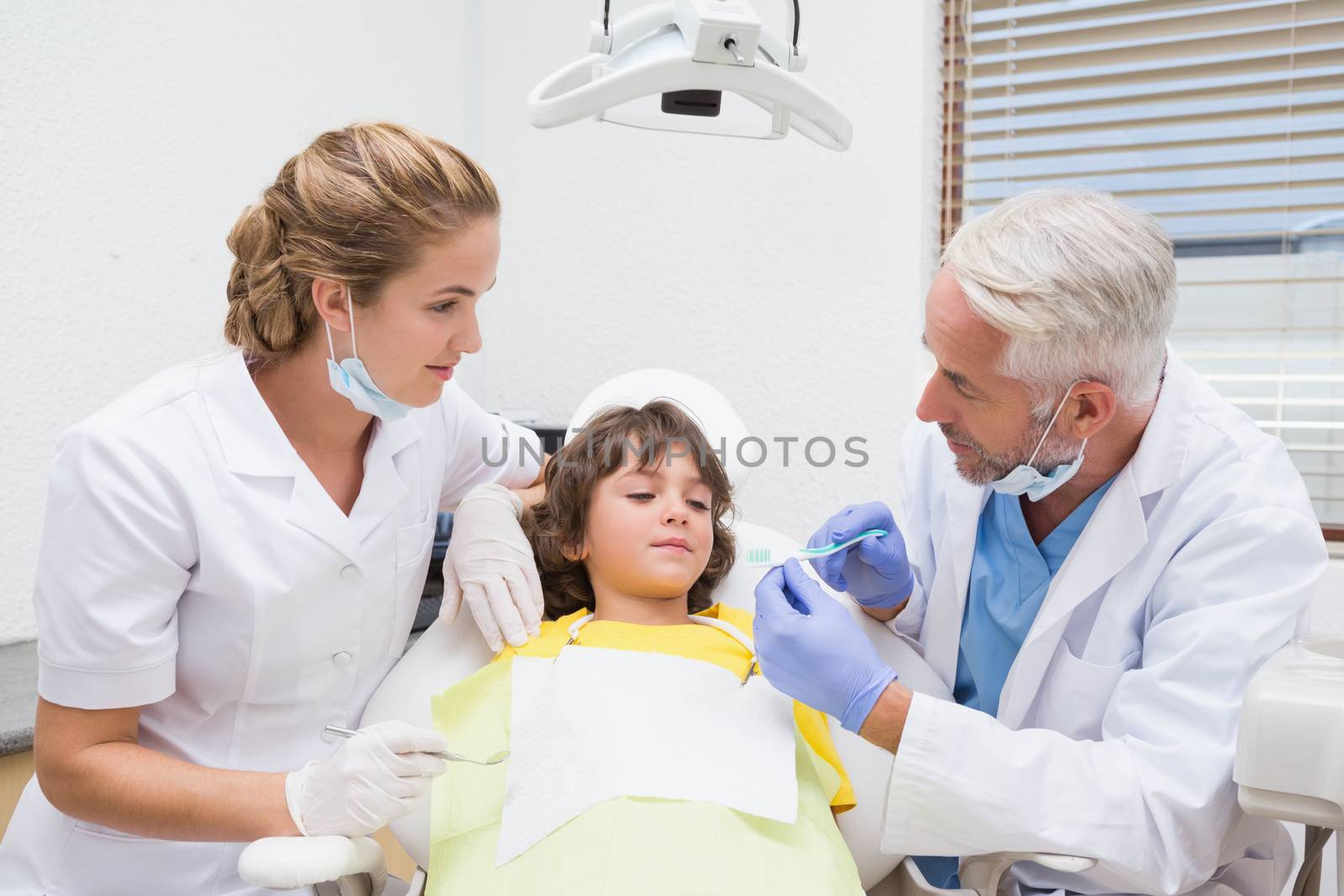 Pediatric dentist showing little boy how to brush his teeth at the dental clinic