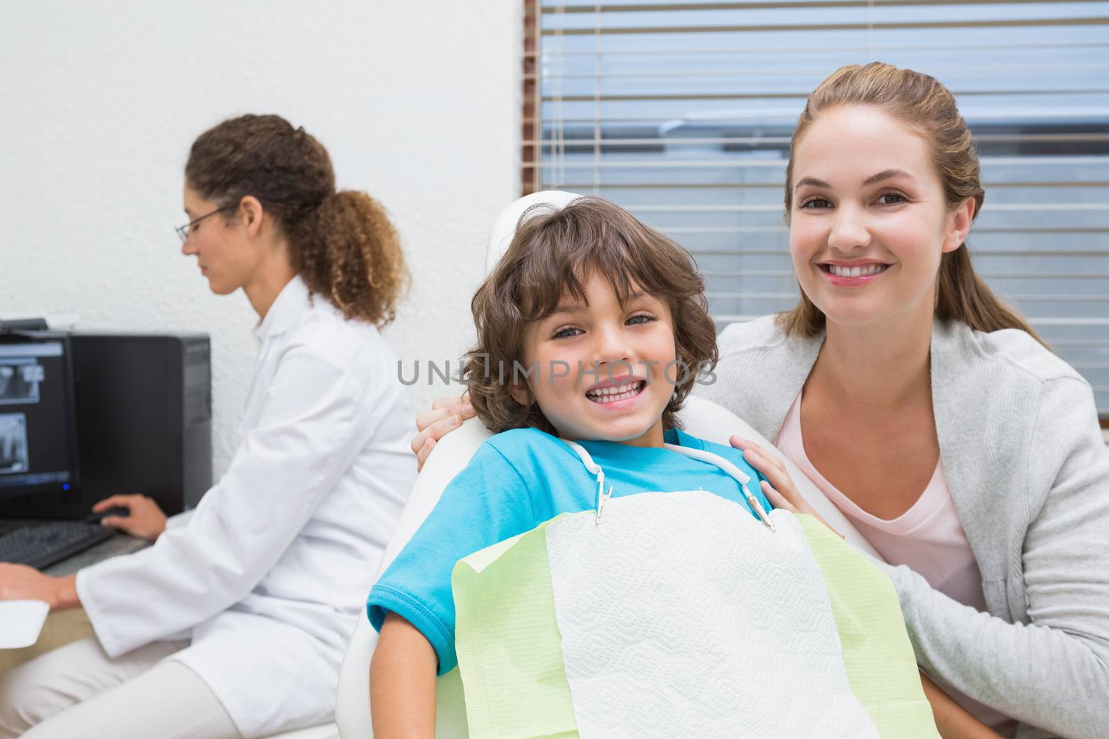 Little boy and mother smiling at camera with dentist in background by Wavebreakmedia