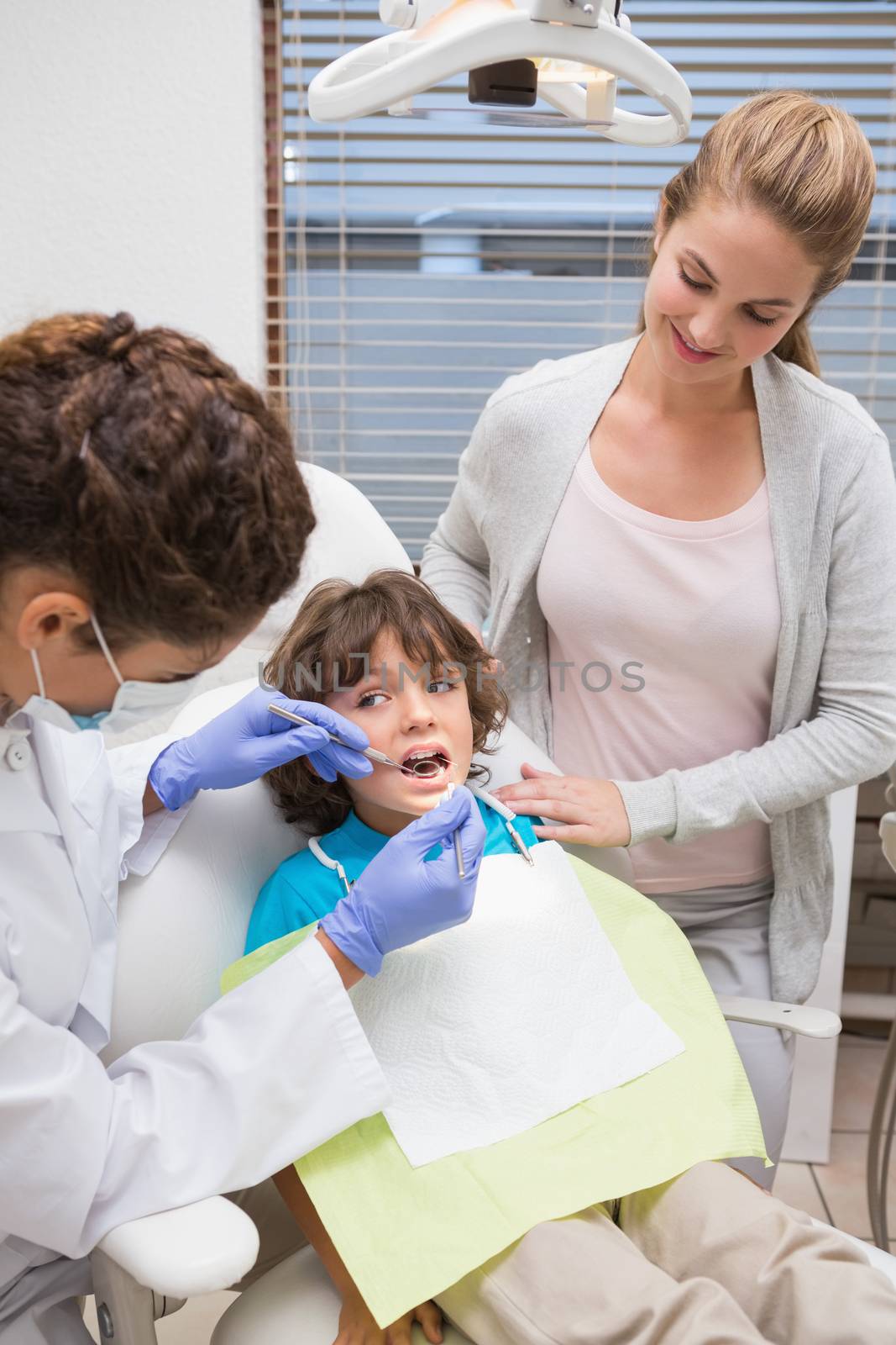 Pediatric dentist examining a little boys teeth with his mother by Wavebreakmedia