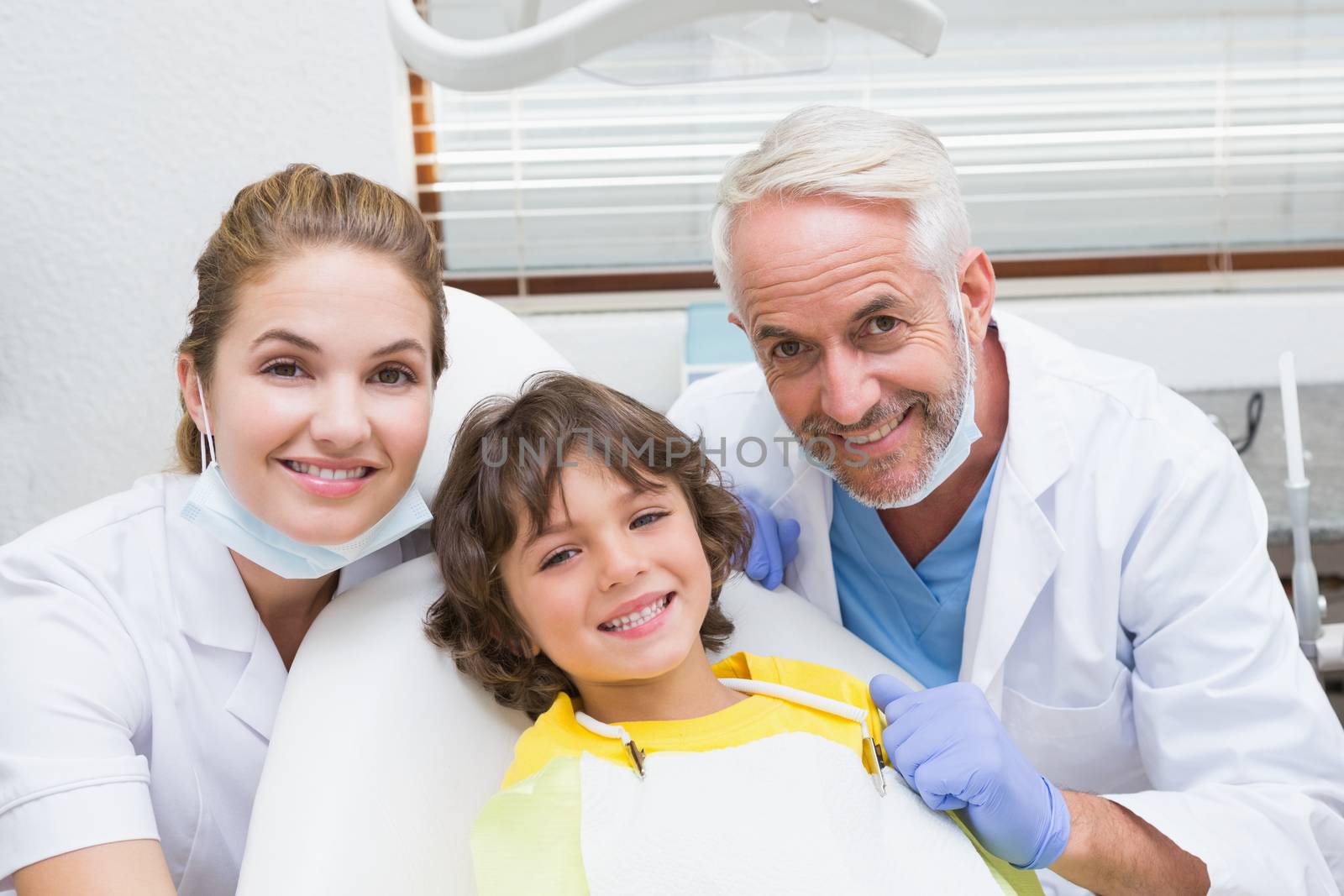 Pediatric dentist assistant and little boy all smiling at camera at the dental clinic