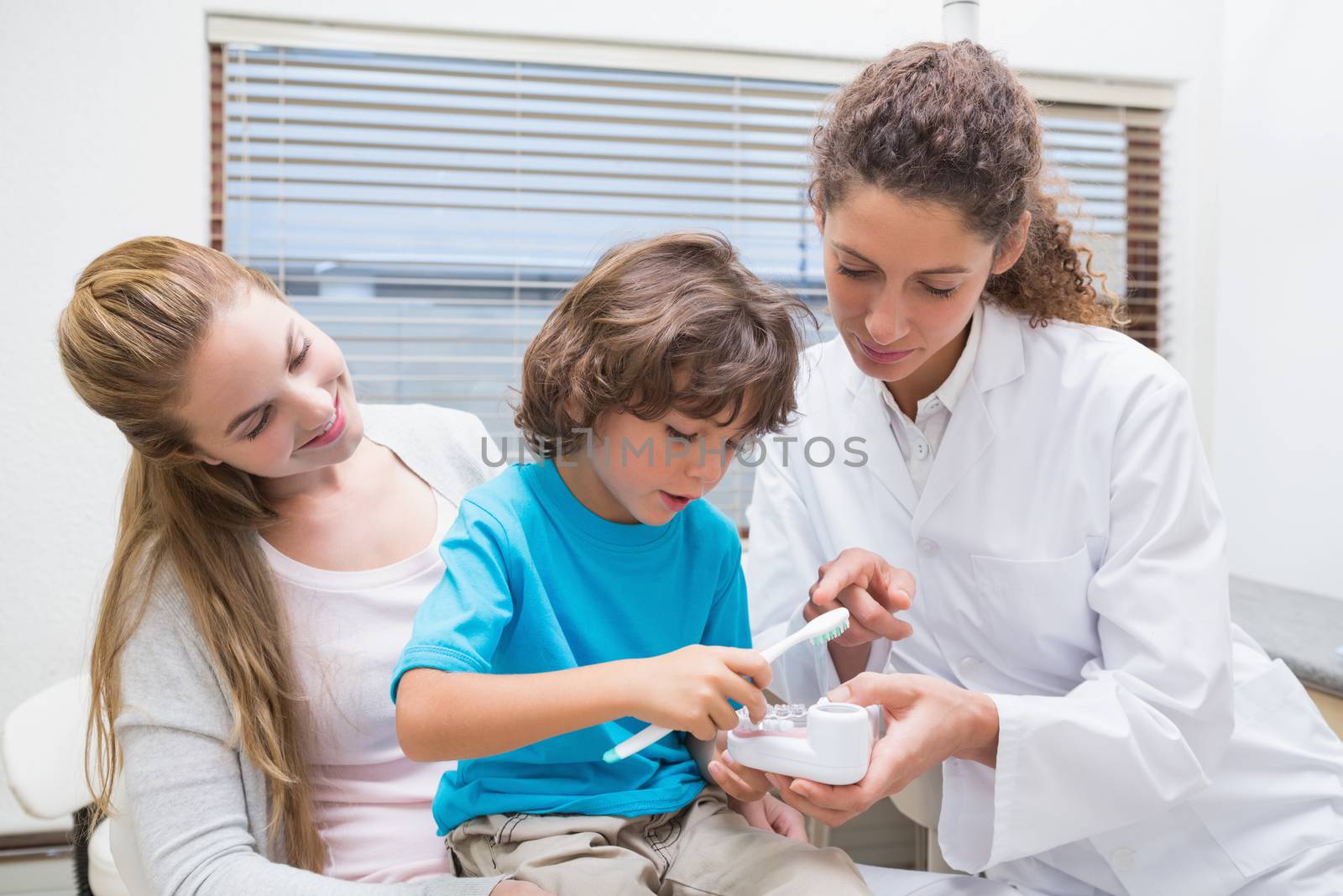 Pediatric dentist showing little boy how to brush teeth with his mother  by Wavebreakmedia