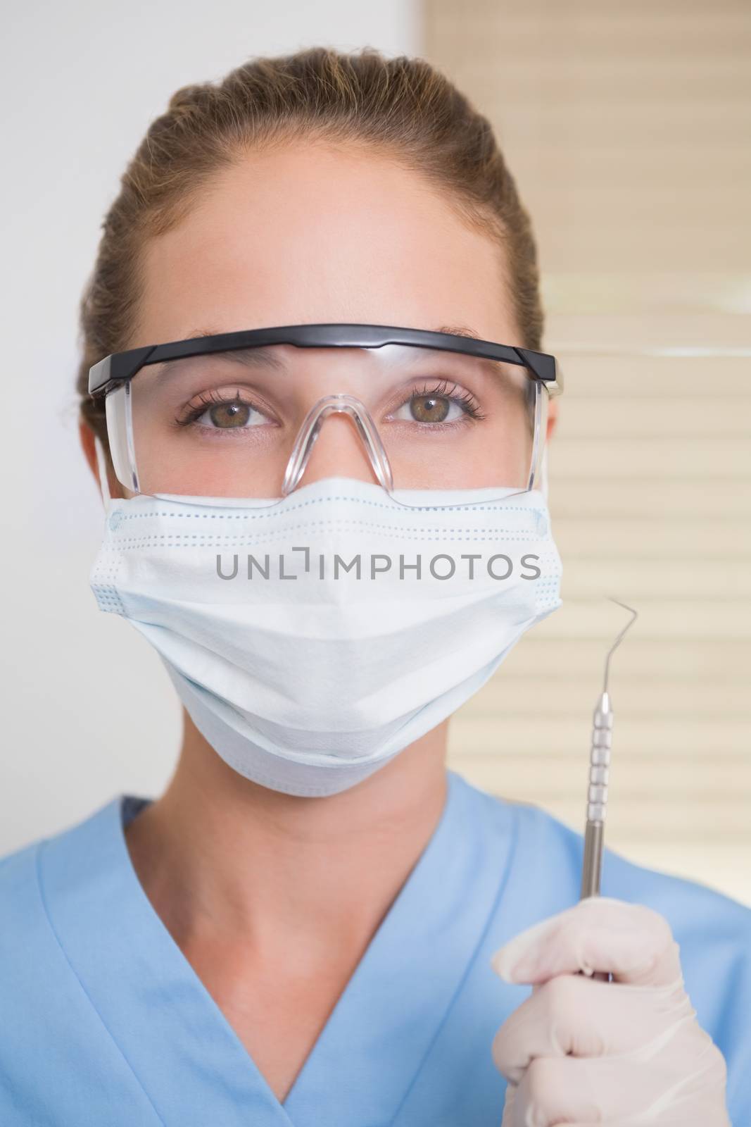 Dentist in surgical mask holding dental explorer by Wavebreakmedia