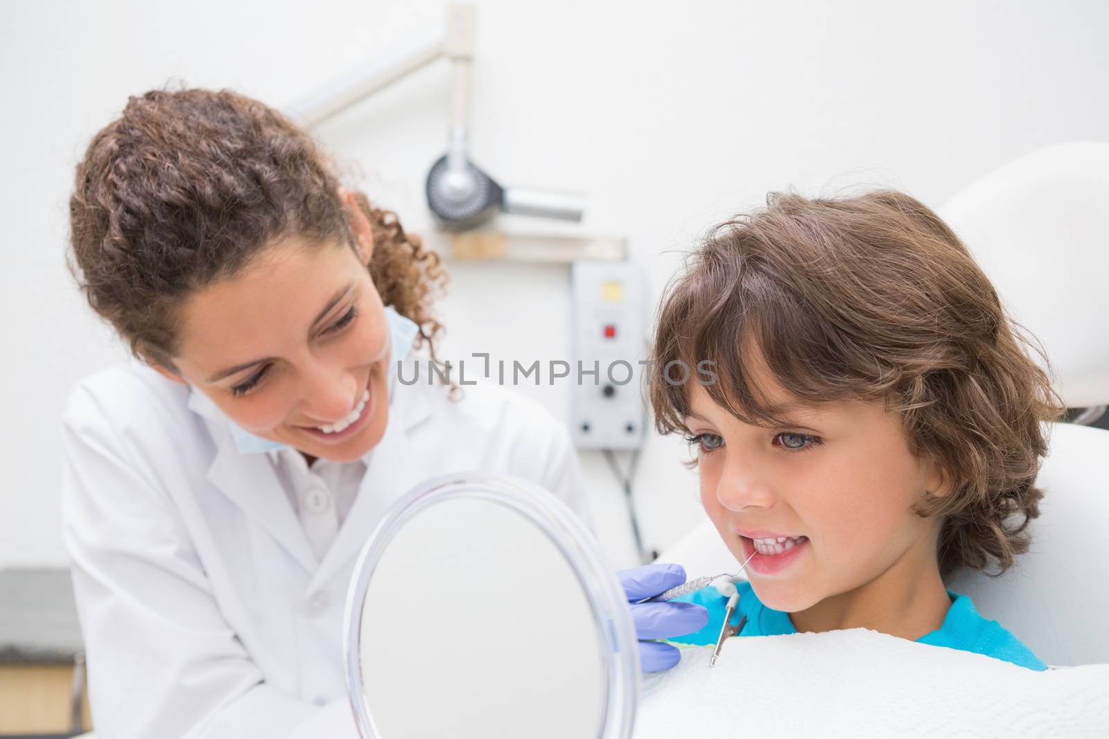 Pediatric dentist showing little boy his teeth in the mirror at the dental clinic