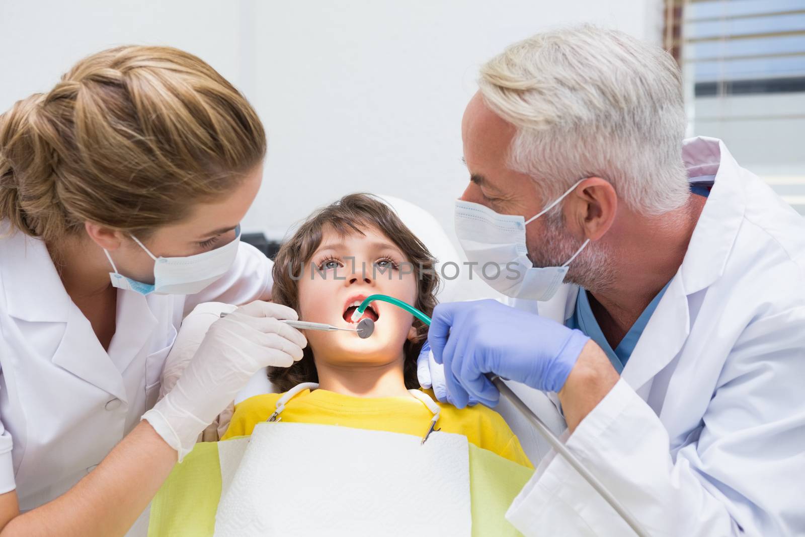 Pediatric dentist examining a little boys teeth with his assistant at the dental clinic