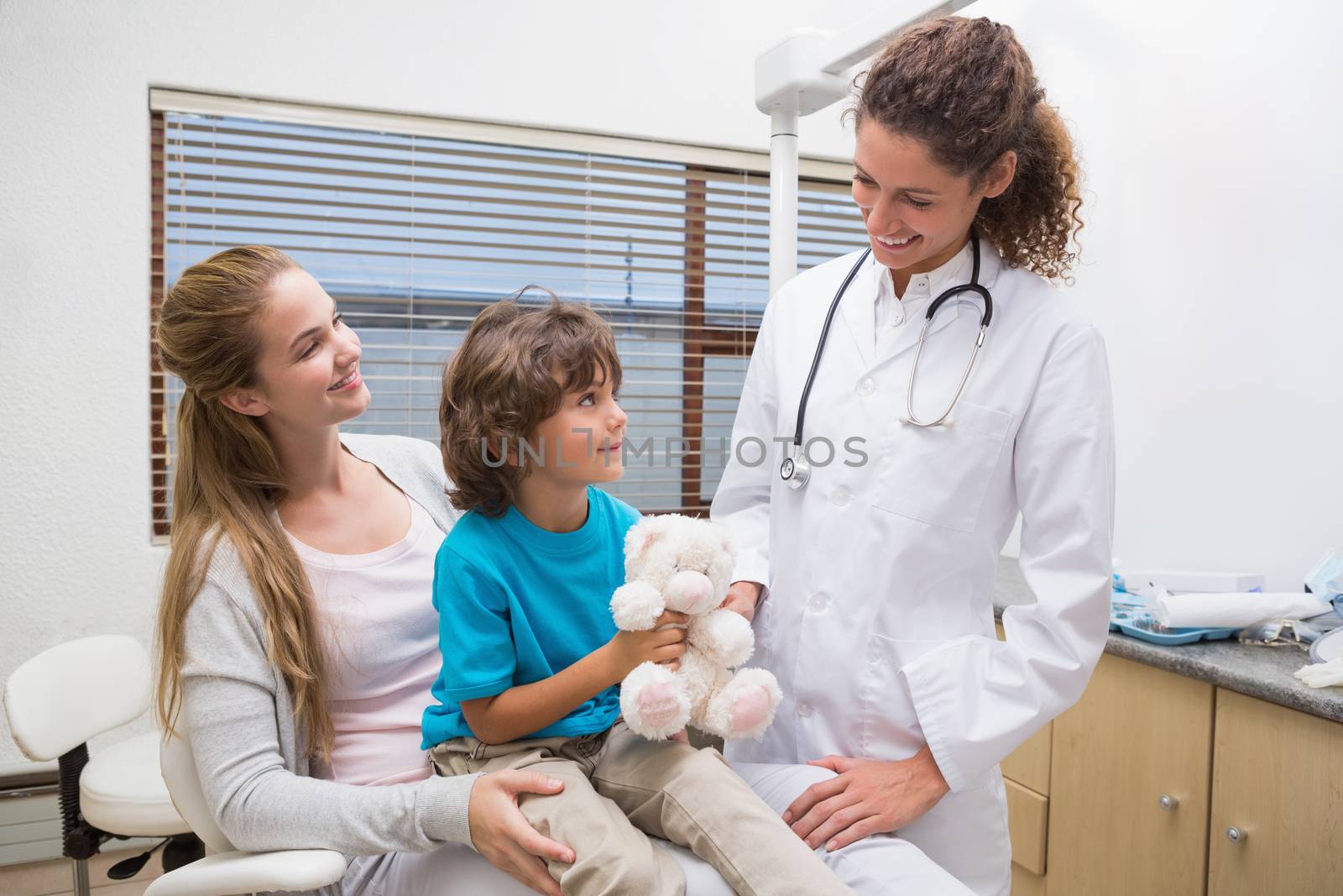 Pediatric dentist smiling at little boy with his mother at the dental clinic