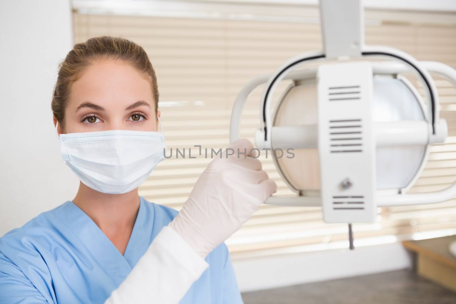 Dentist in surgical mask adjusting light at the dental clinic