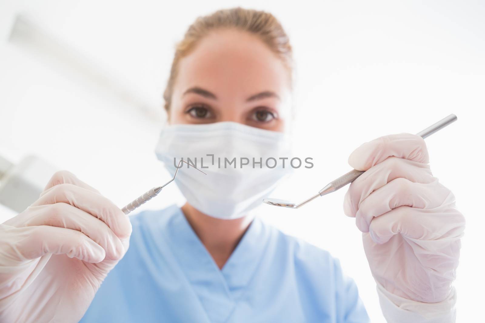 Dentist in surgical mask holding tools over patient by Wavebreakmedia
