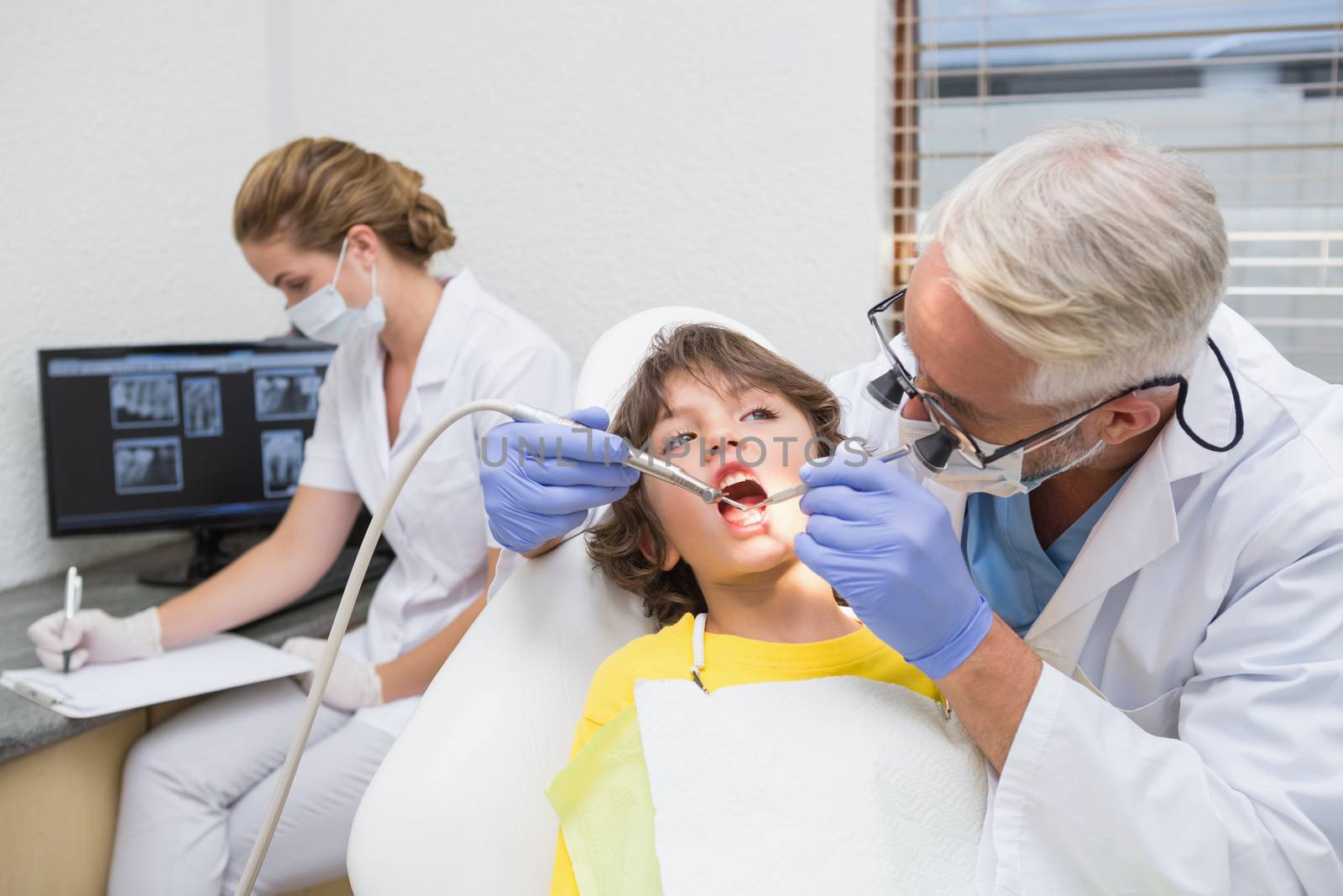 Pediatric dentist examining a little boys teeth with assistant behind by Wavebreakmedia