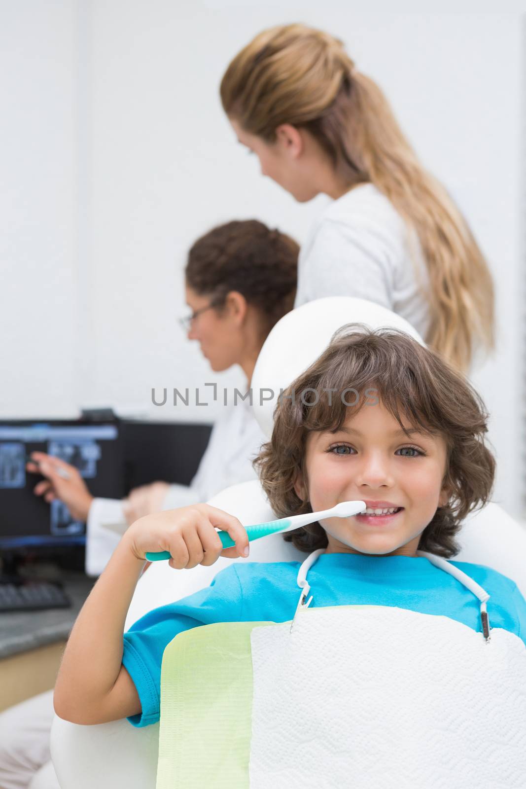 Little boy smiling at camera with mother and dentist in background at the dental clinic