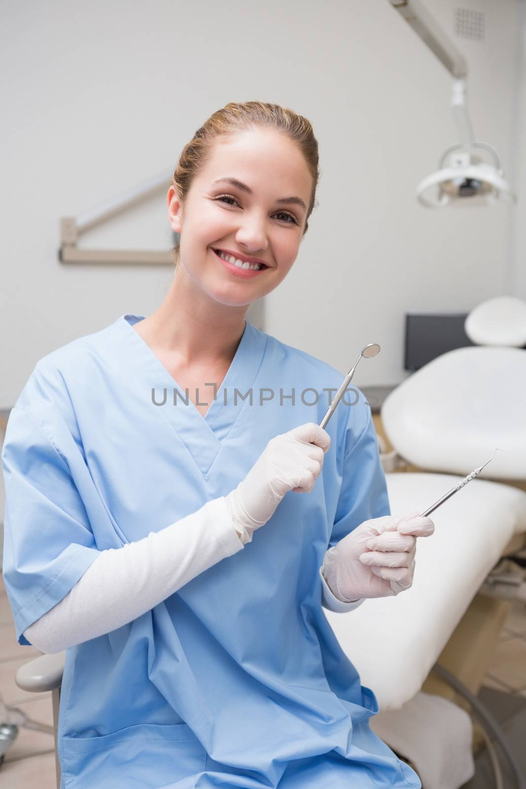Dentist in blue scrubs smiling at camera holding tools at the dental clinic
