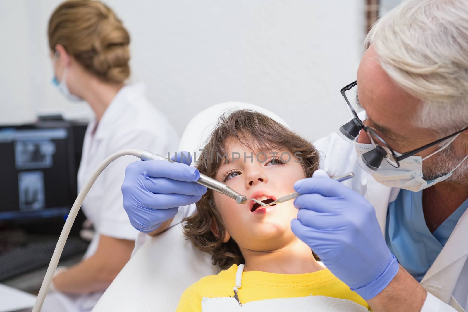Pediatric dentist examining a little boys teeth with assistant behind at the dental clinic