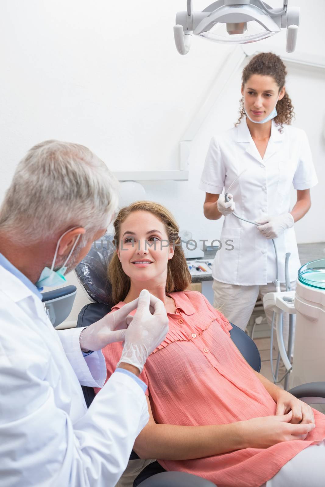 Dentist examining a patients teeth in the dentists chair with assistant by Wavebreakmedia