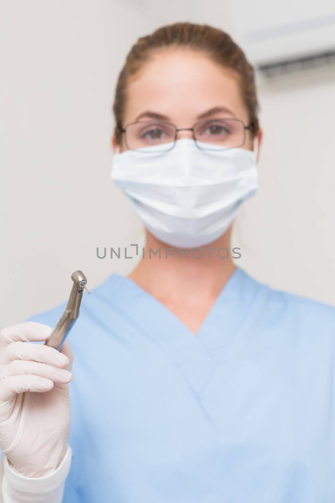 Dentist in blue scrubs holding drill looking at camera at the dental clinic