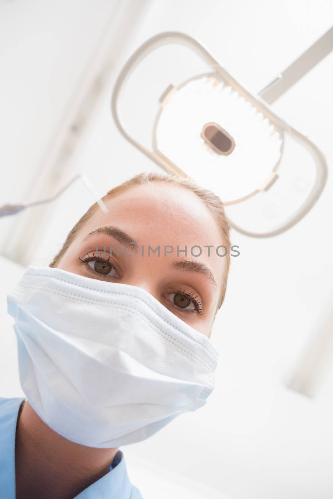 Dentist in surgical mask holding dental explorer over patient by Wavebreakmedia