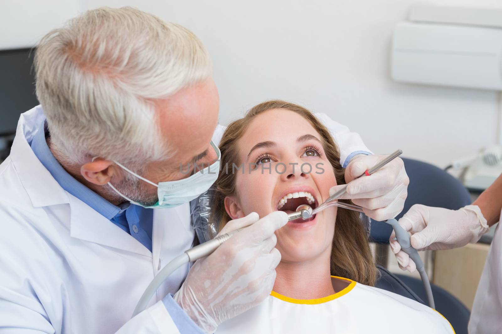 Dentist examining a patients teeth in the dentists chair with assistant at the dental clinic