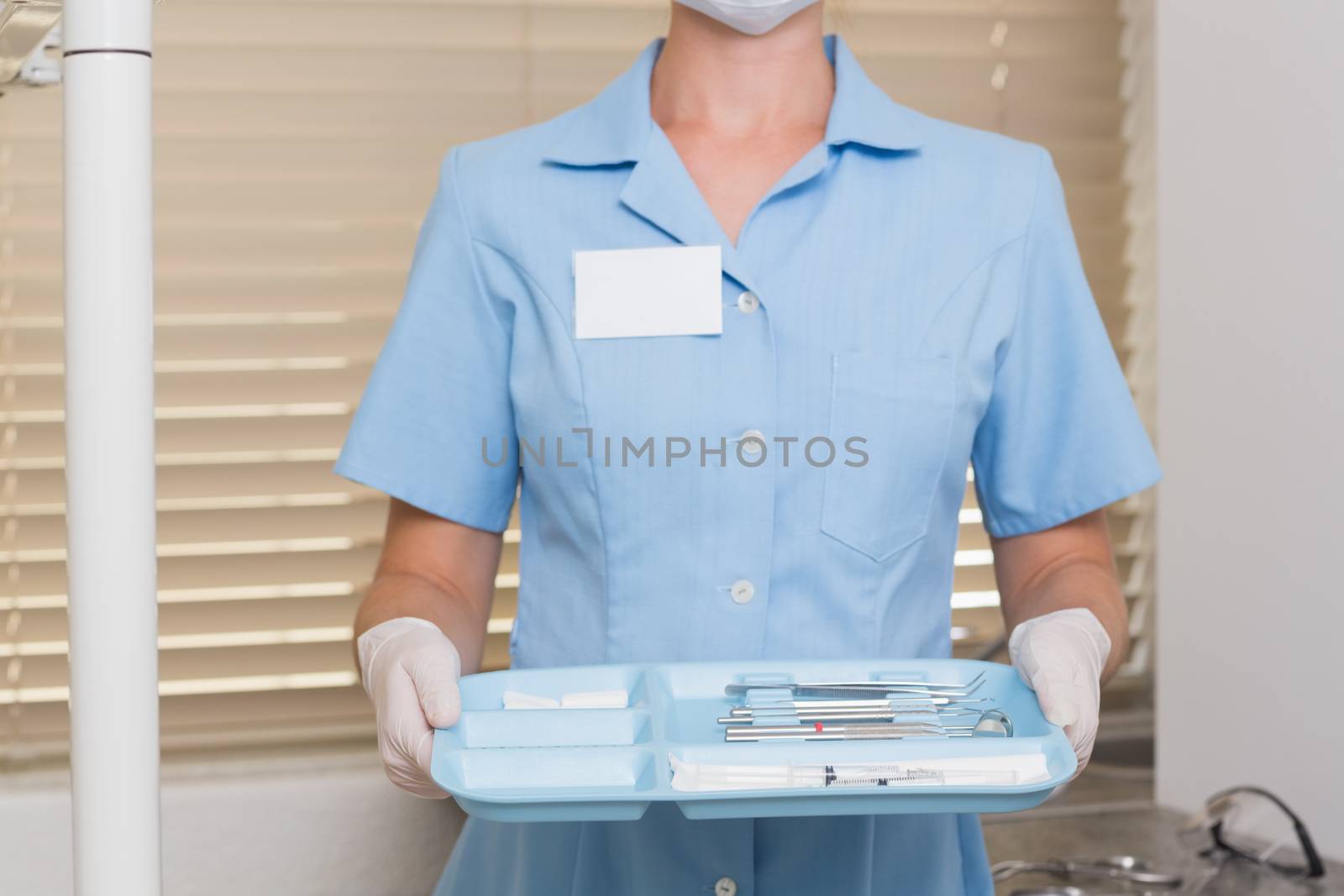 Dental assistant in blue holding tray of tools at the dental clinic