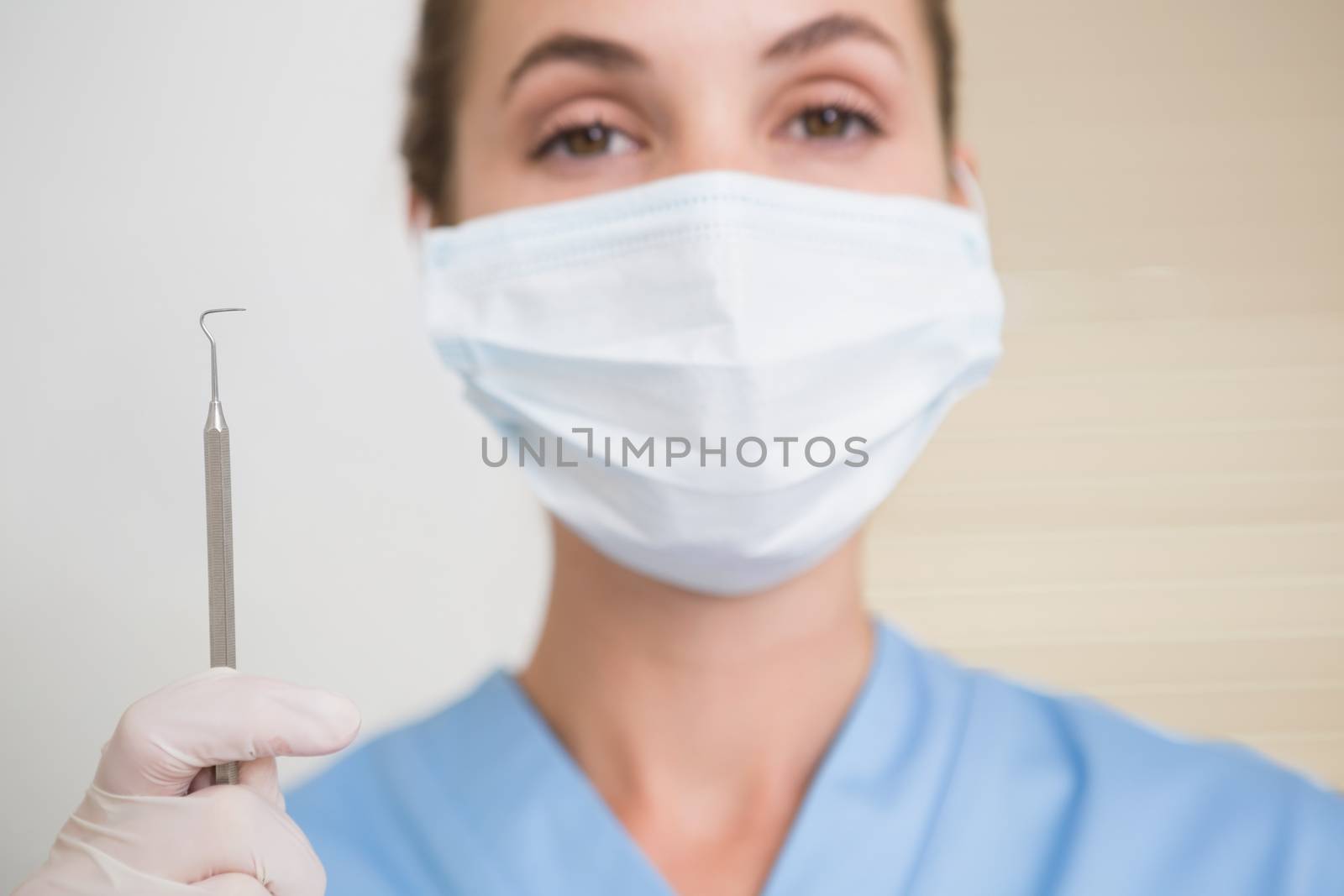 Dentist in surgical mask holding dental explorer by Wavebreakmedia
