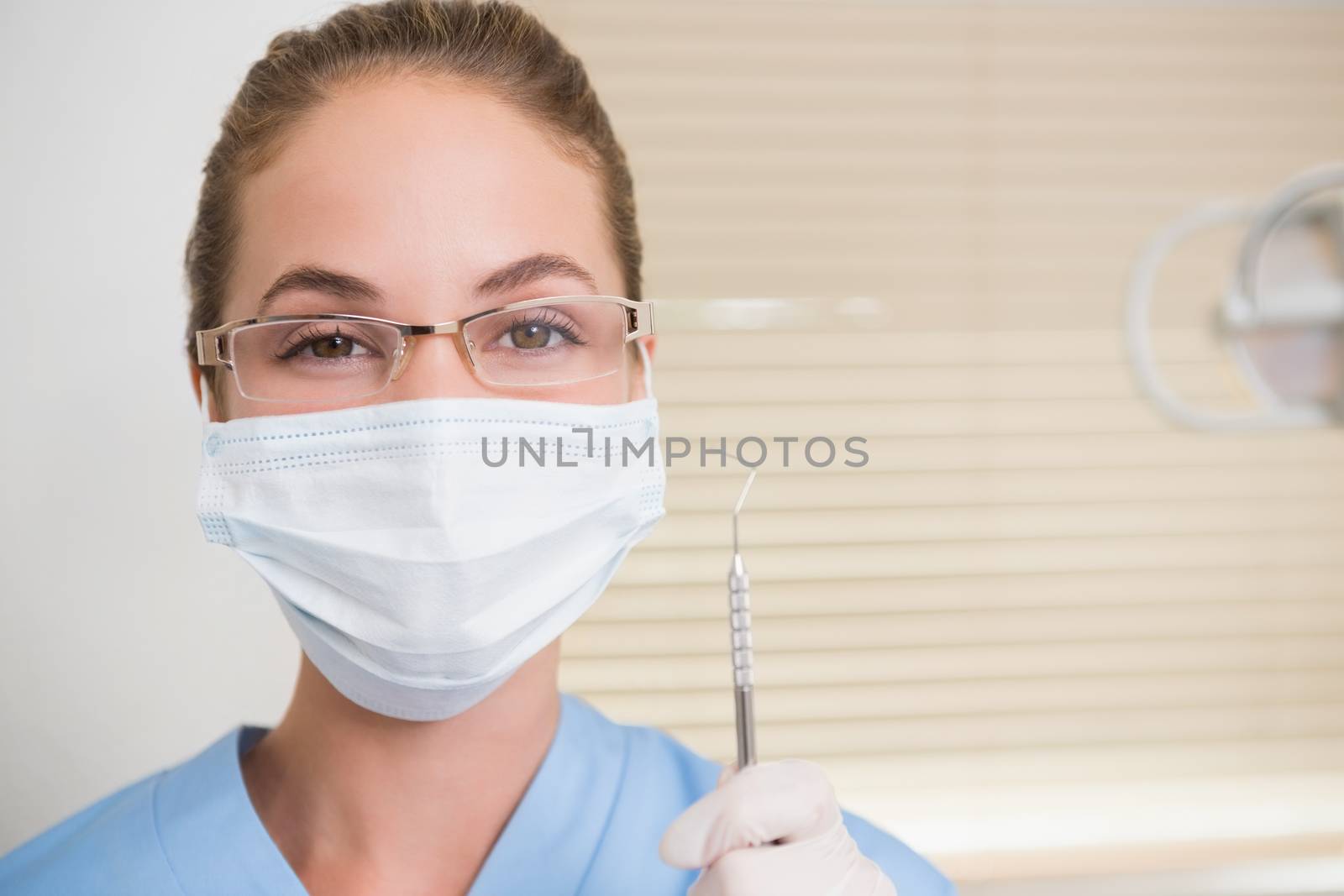 Dentist in surgical mask holding dental explorer at the dental clinic
