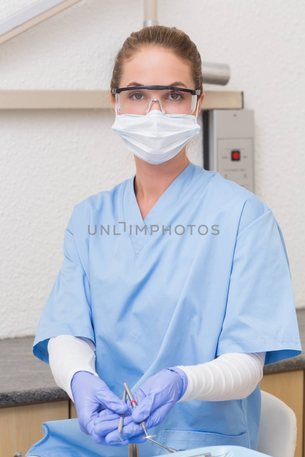 Dentist in blue scrubs holding dental tools by Wavebreakmedia
