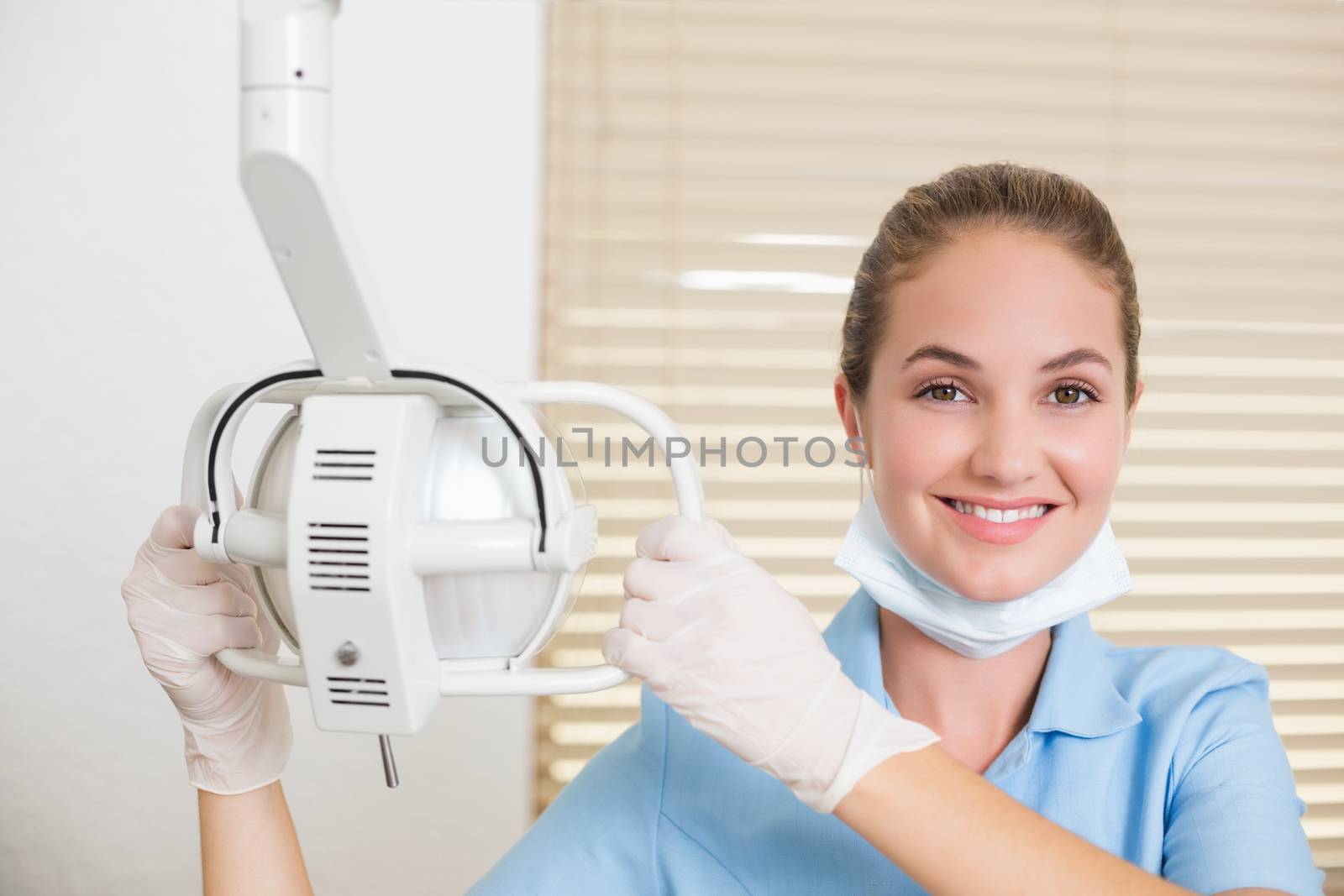 Dental assistant smiling at camera beside light at the dental clinic