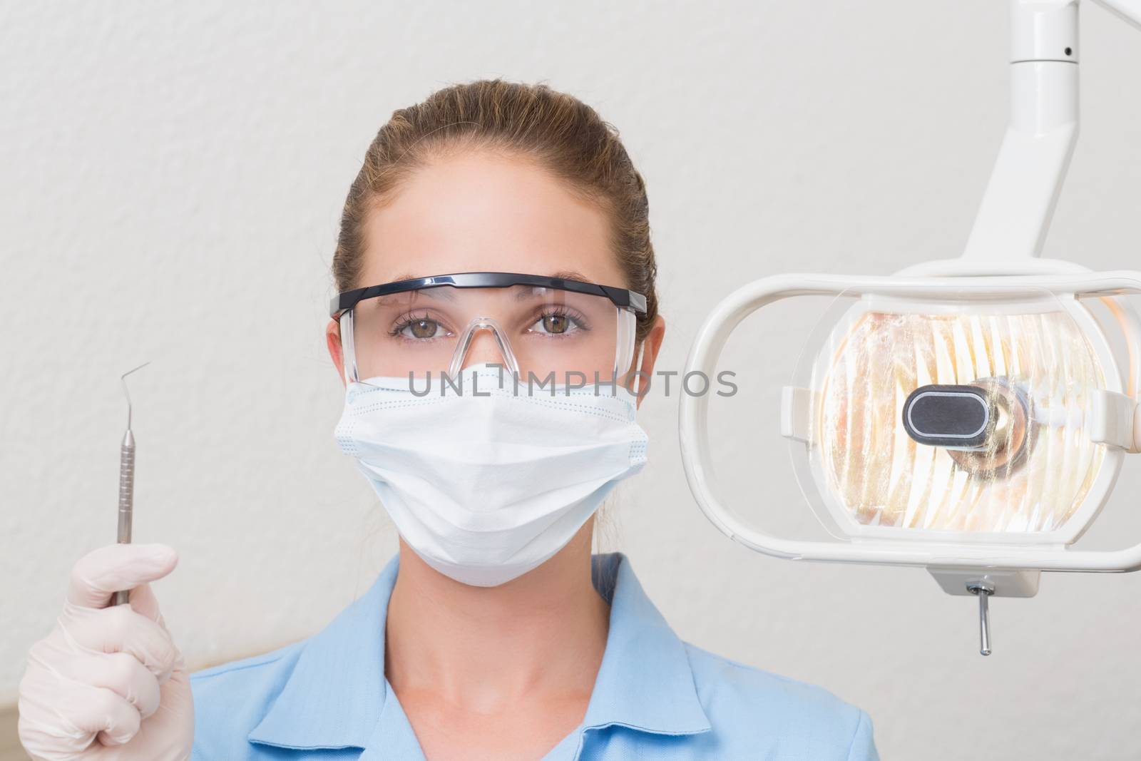 Dental assistant in mask holding dental explorer at the dental clinic