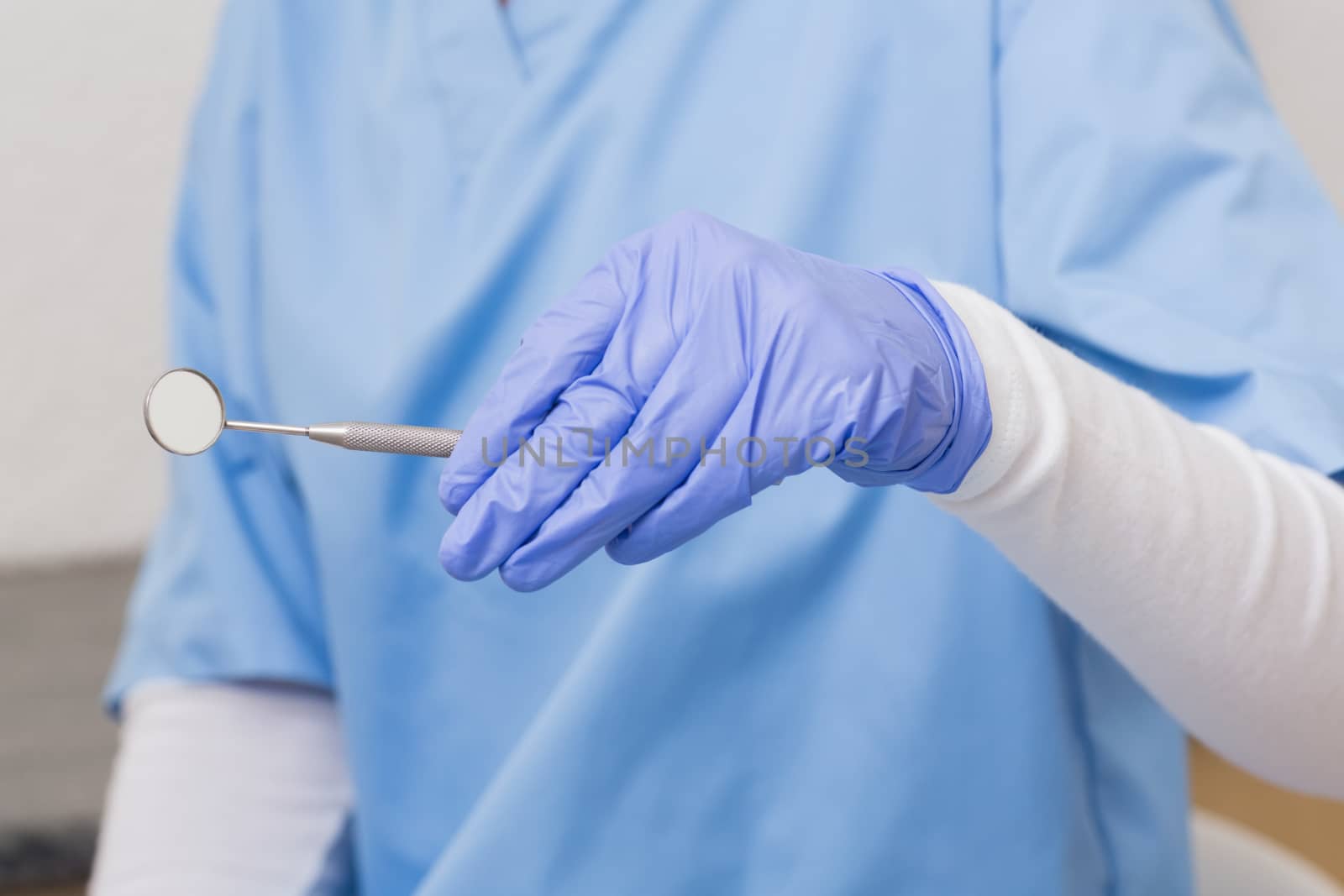 Dentist in blue scrubs holding angled mirror at the dental clinic