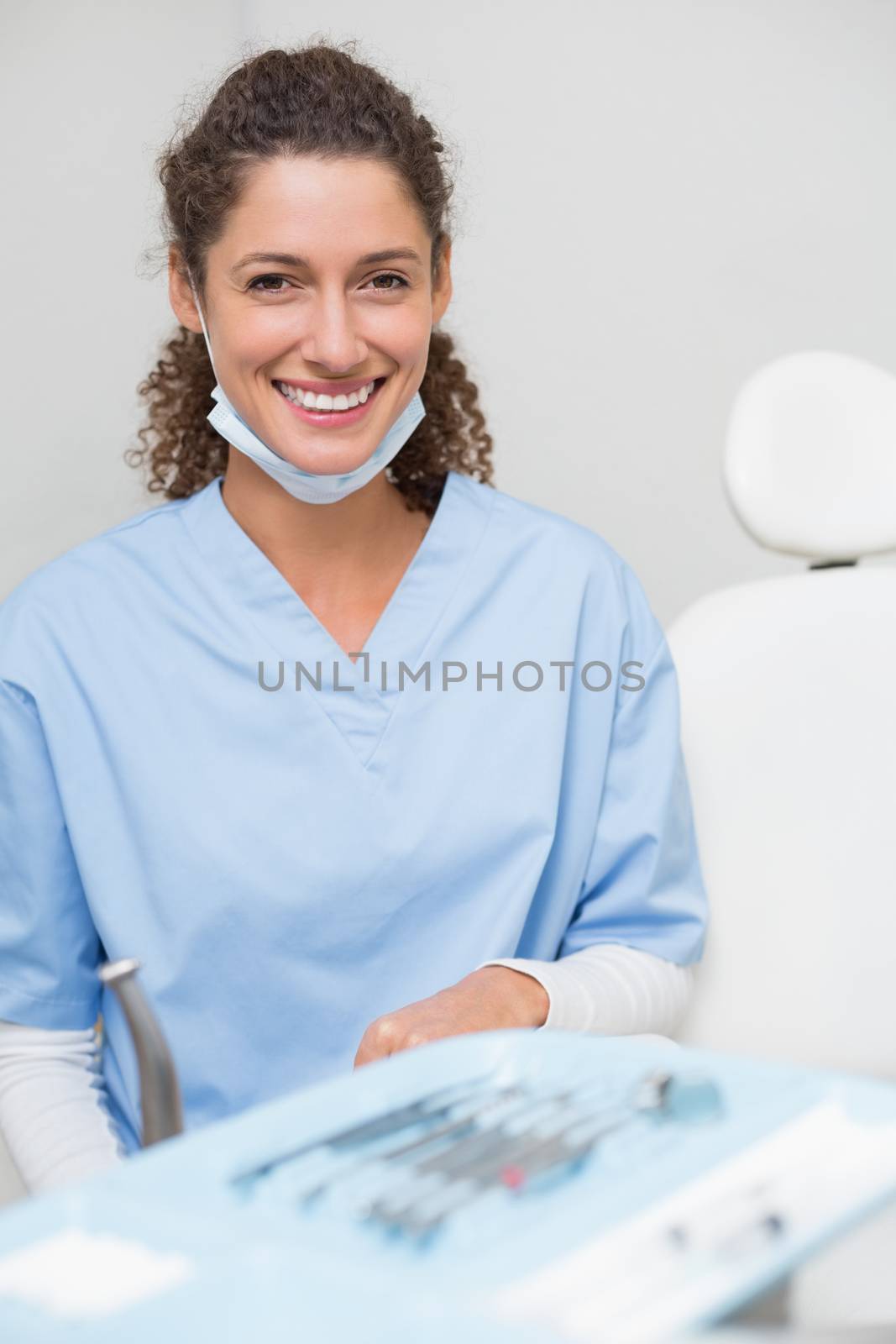 Dentist smiling at camera beside chair at the dental clinic