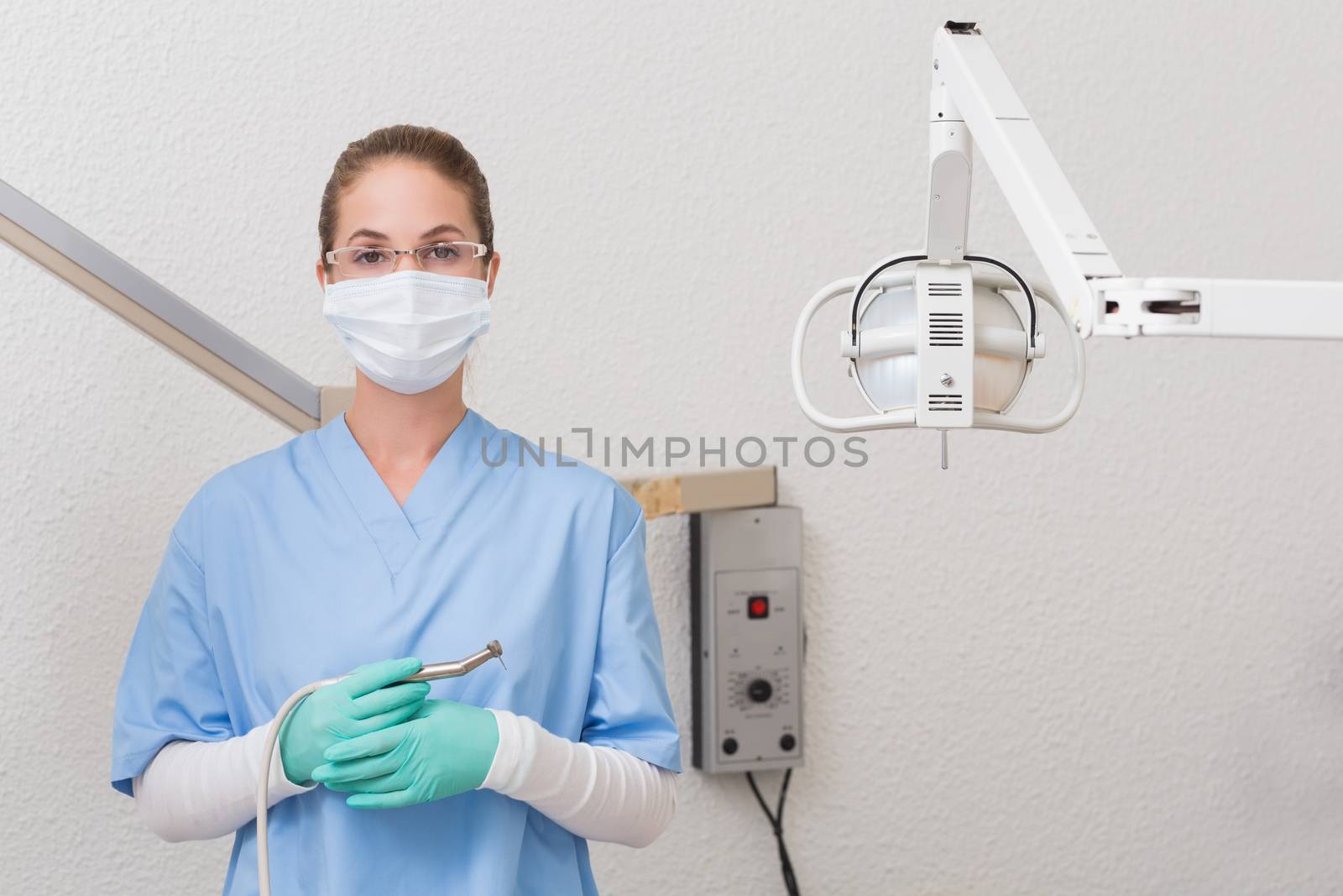 Dentist in blue scrubs holding dental drill looking at camera at the dental clinic