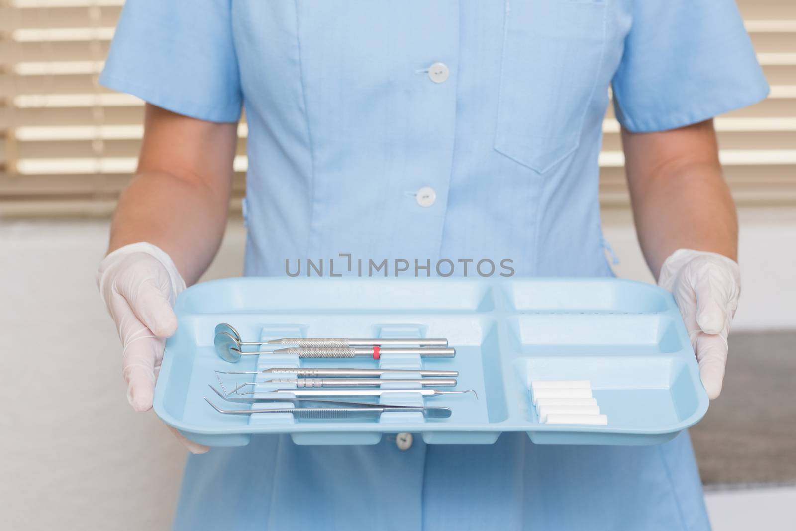 Dental assistant in blue holding tray of tools at the dental clinic