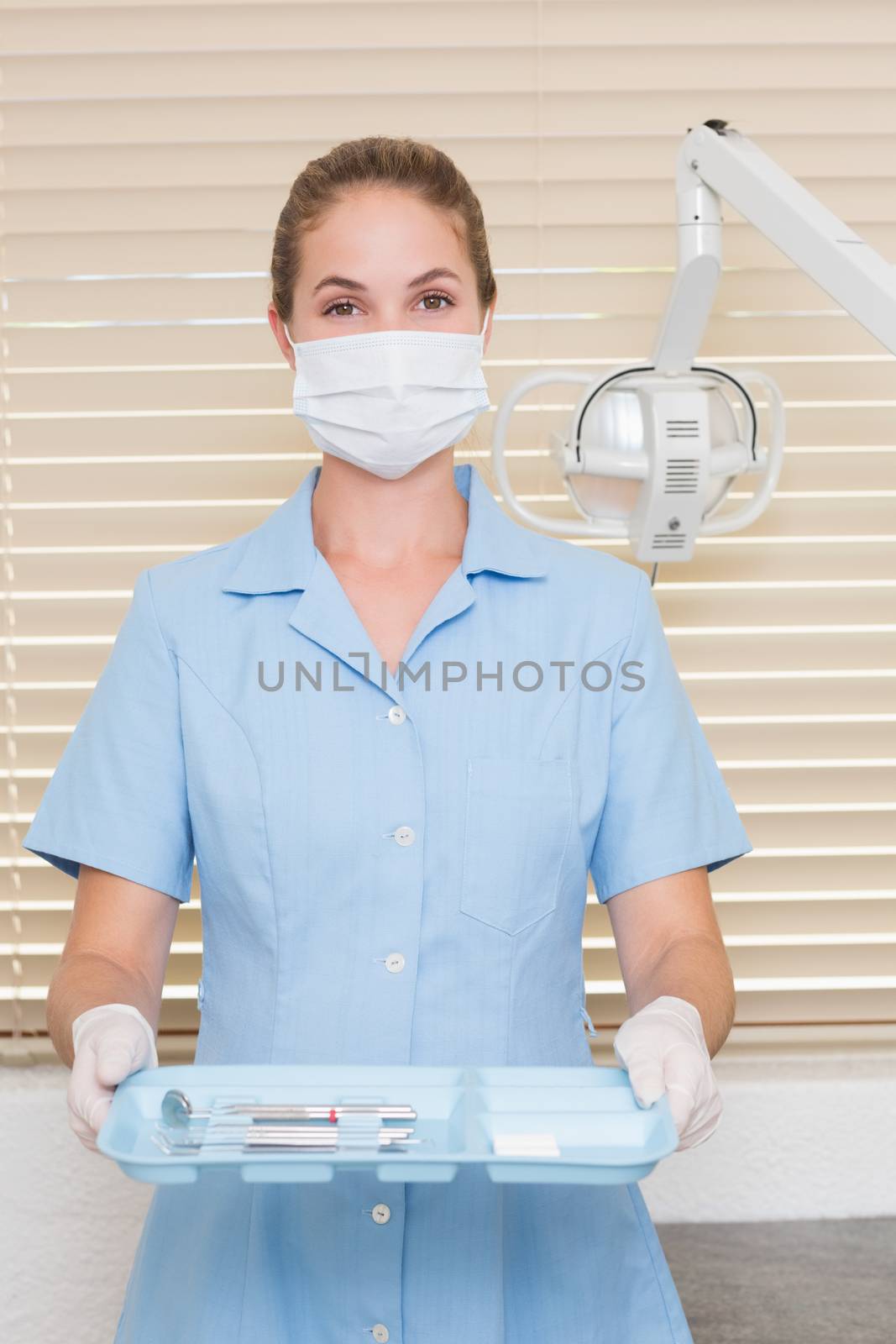 Dental assistant in mask holding tray of tools at the dental clinic