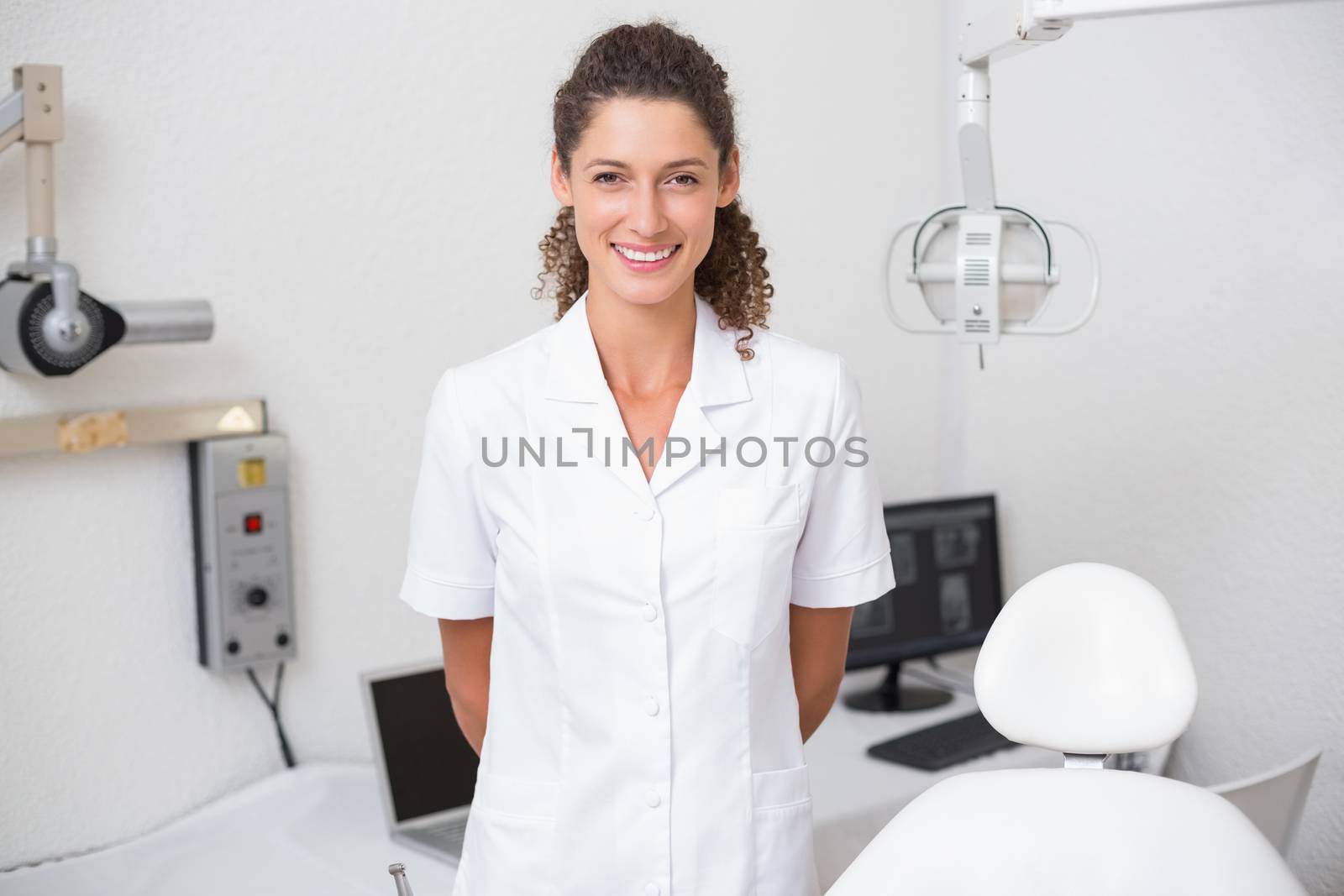 Dental assistant smiling at camera beside chair at the dental clinic