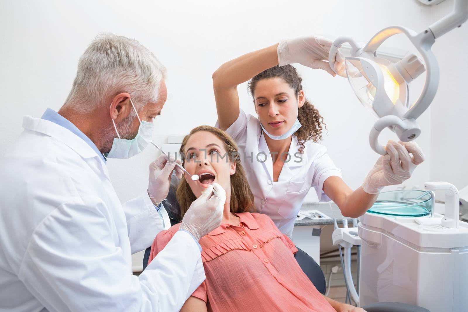 Dentist examining a patients teeth in the dentists chair with assistant by Wavebreakmedia