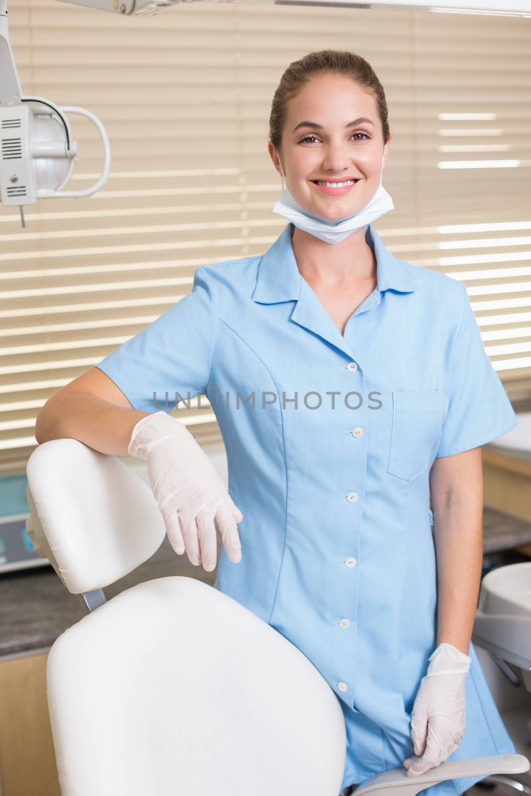 Dental assistant smiling at camera beside chair at the dental clinic