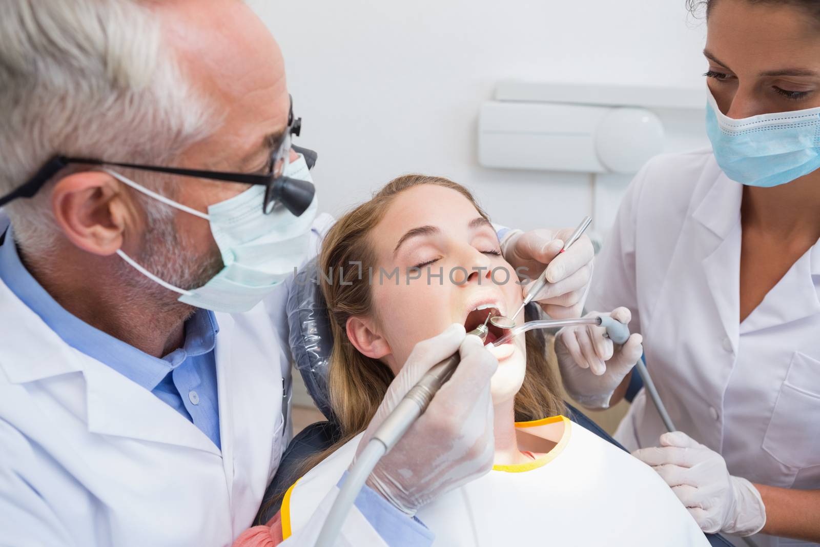 Dentist examining a patients teeth in the dentists chair with assistant at the dental clinic