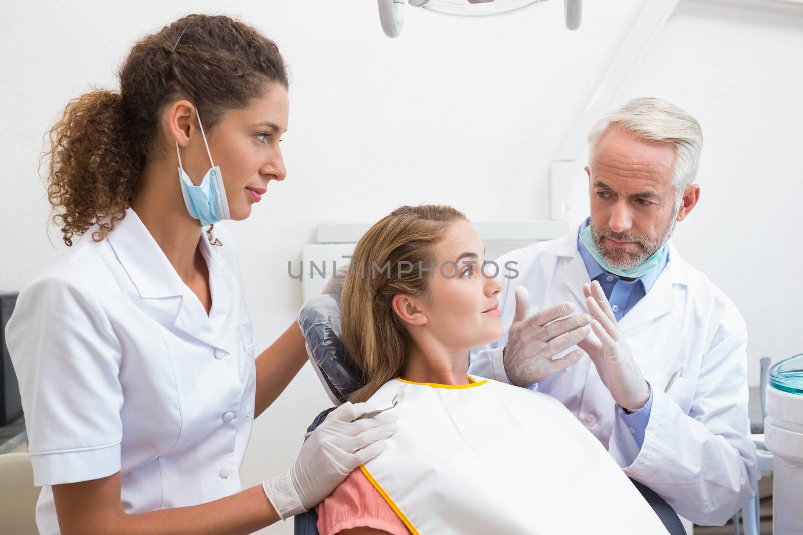 Dentist examining a patients teeth in the dentists chair with assistant by Wavebreakmedia