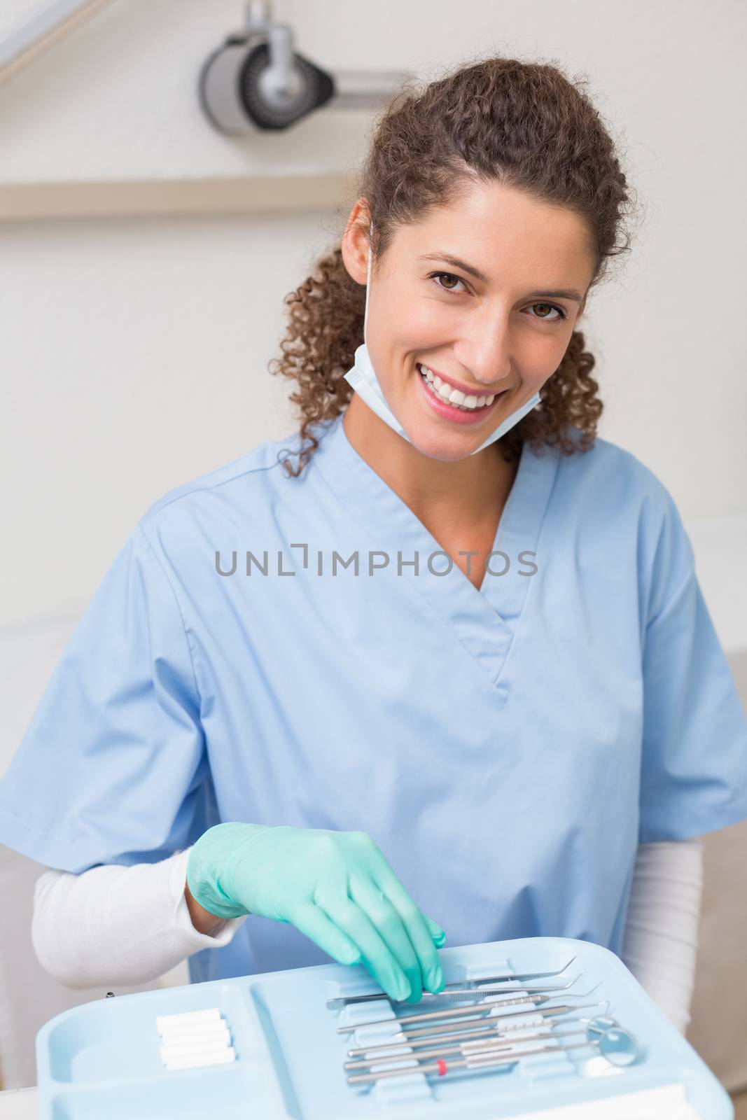 Dentist smiling at camera while picking up tools at the dental clinic