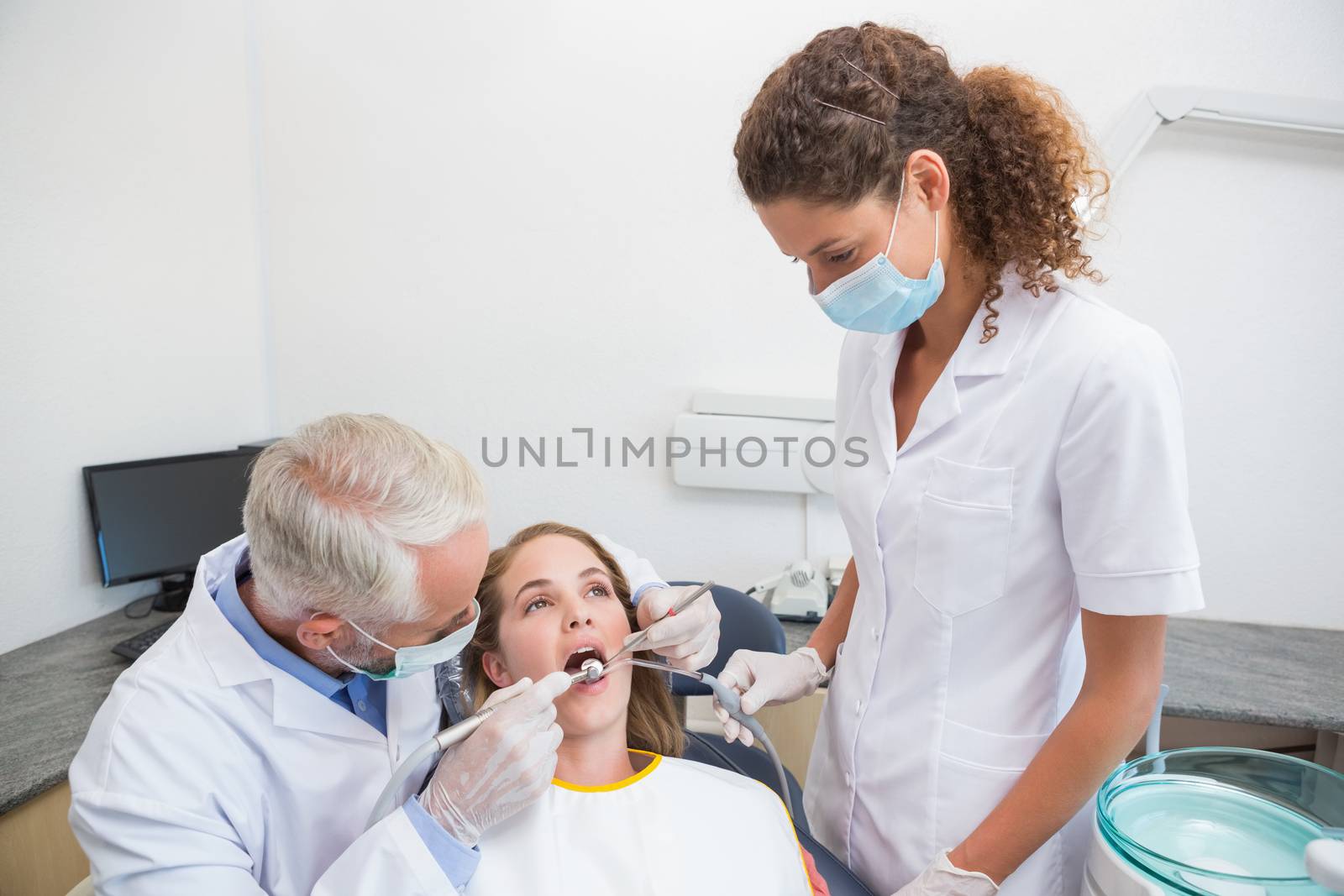 Dentist examining a patients teeth in the dentists chair with assistant at the dental clinic