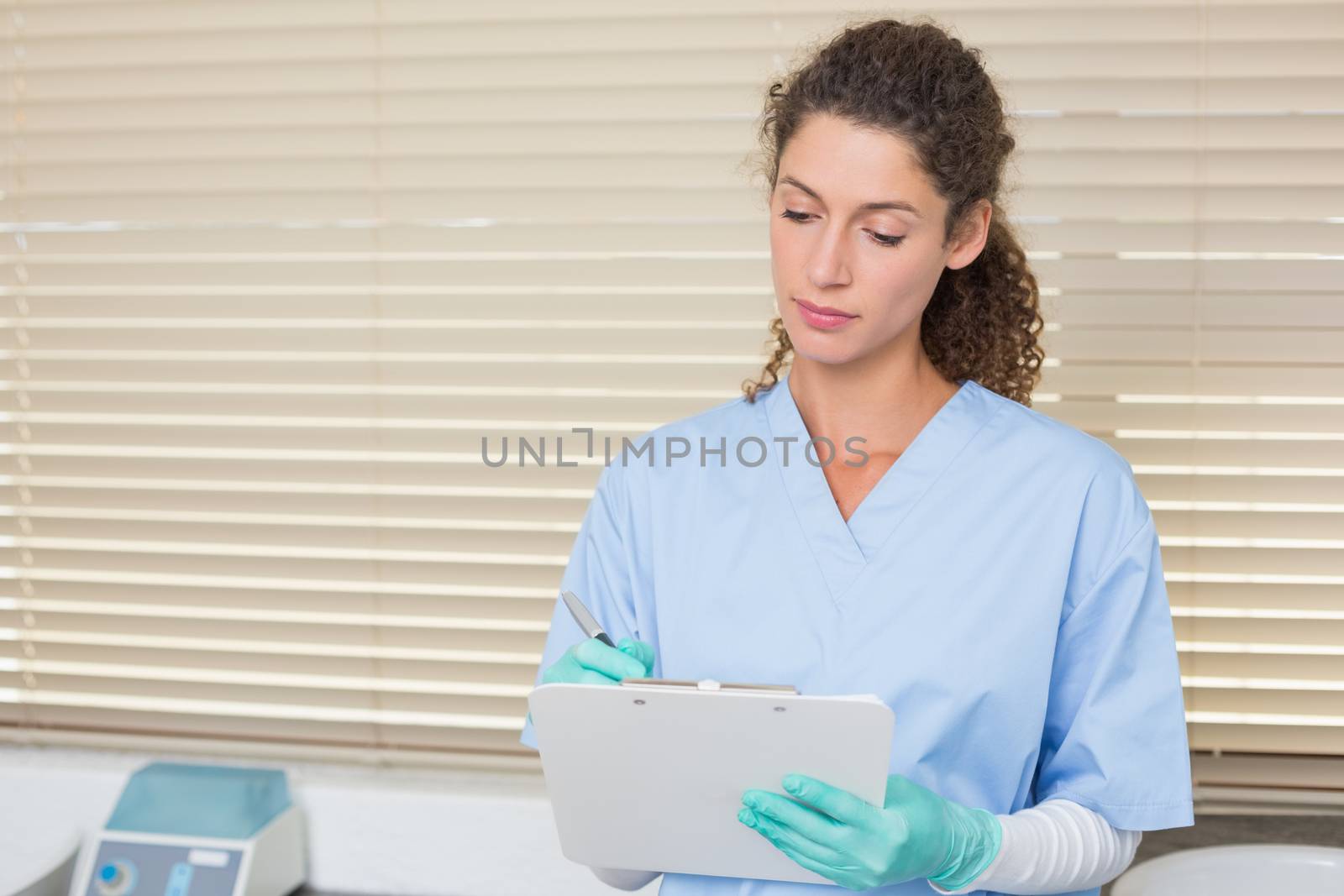 Dentist in blue scrubs writing on clipboard by Wavebreakmedia