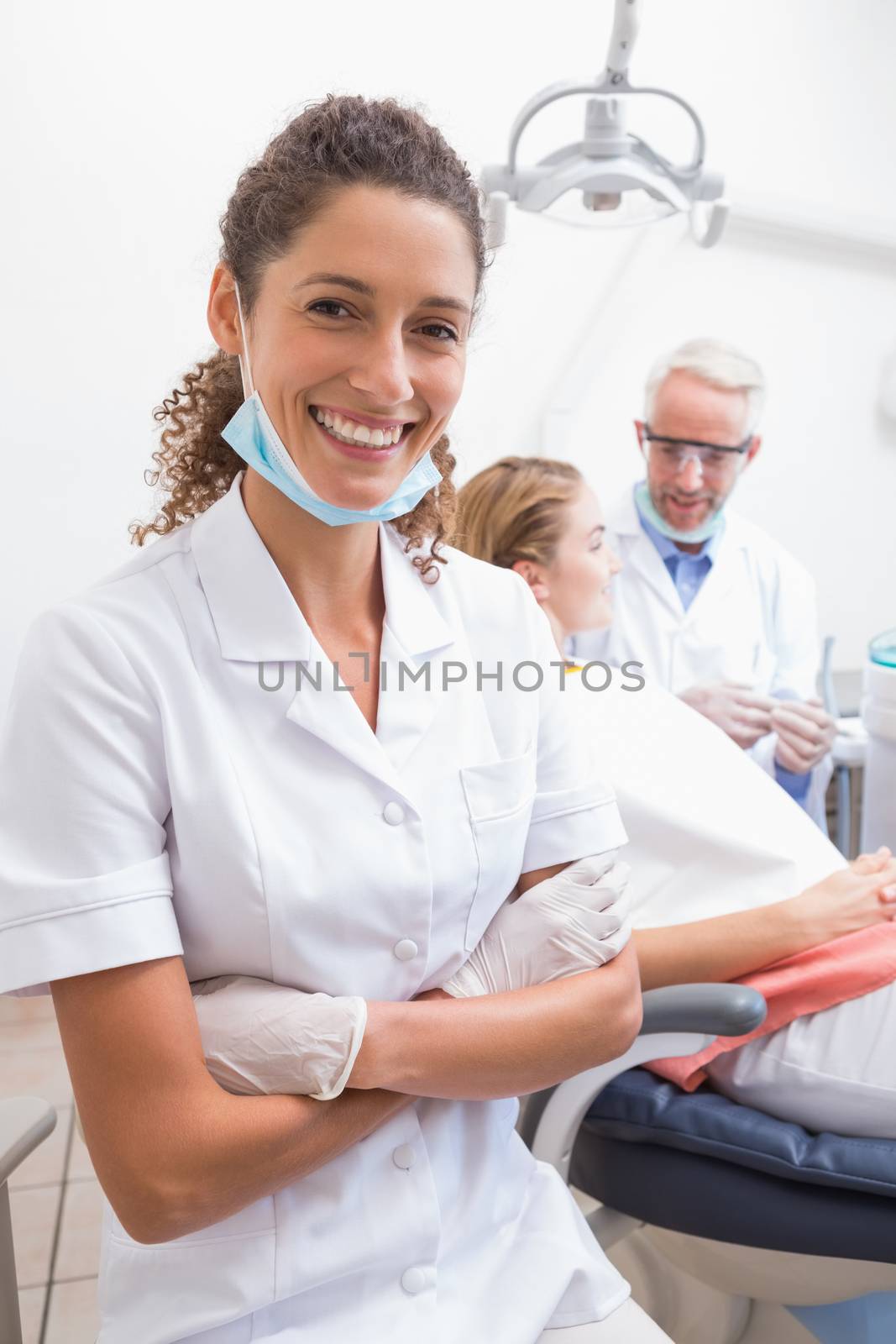 Dental assistant smiling at camera with dentist and patient behind at the dental clinic