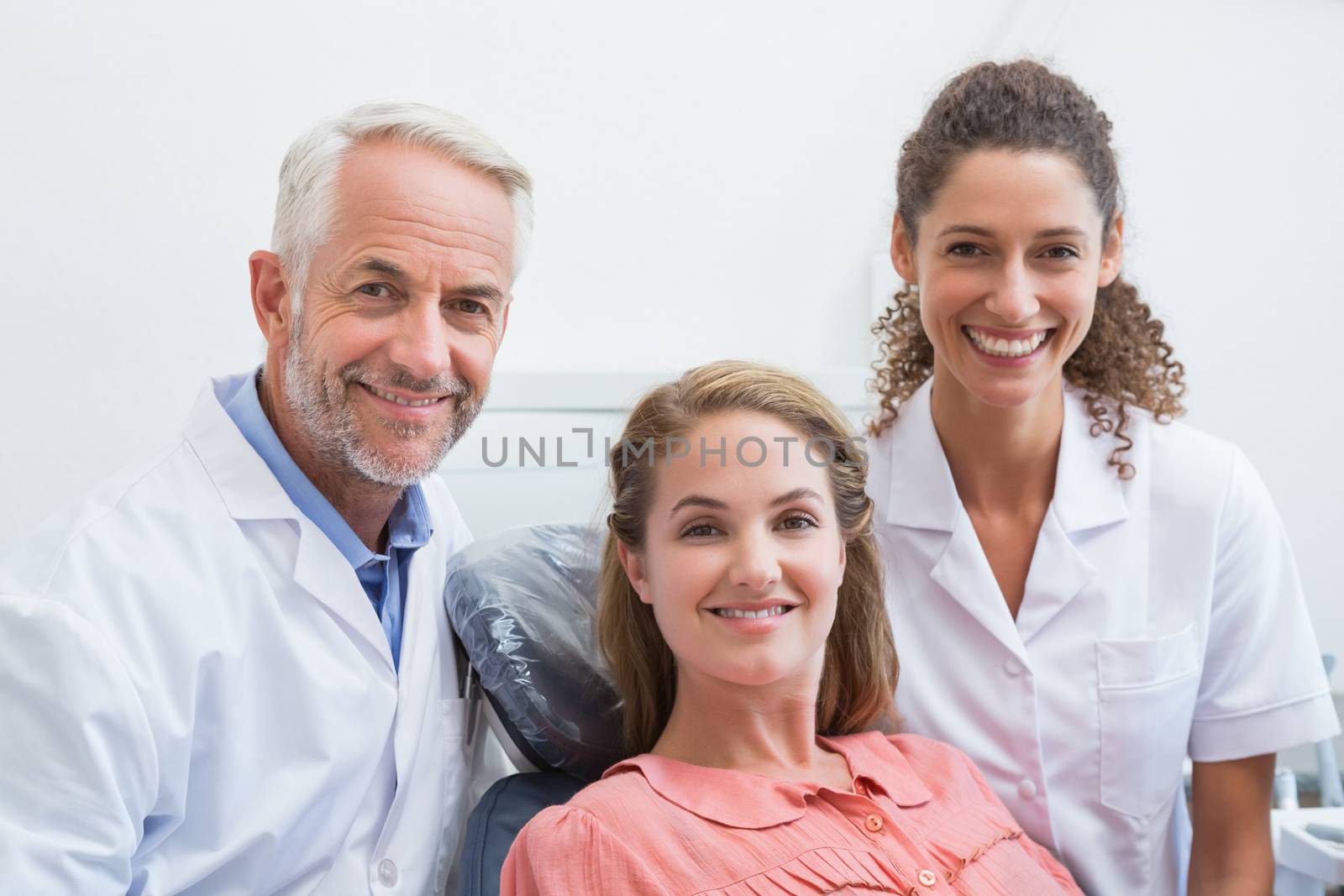 Dentist his assistant and patient all smiling at camera at the dental clinic