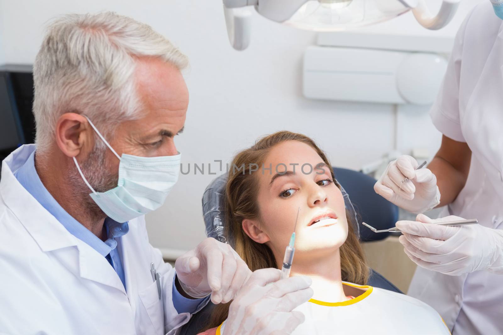 Dentist examining a patients teeth in the dentists chair with assistant by Wavebreakmedia