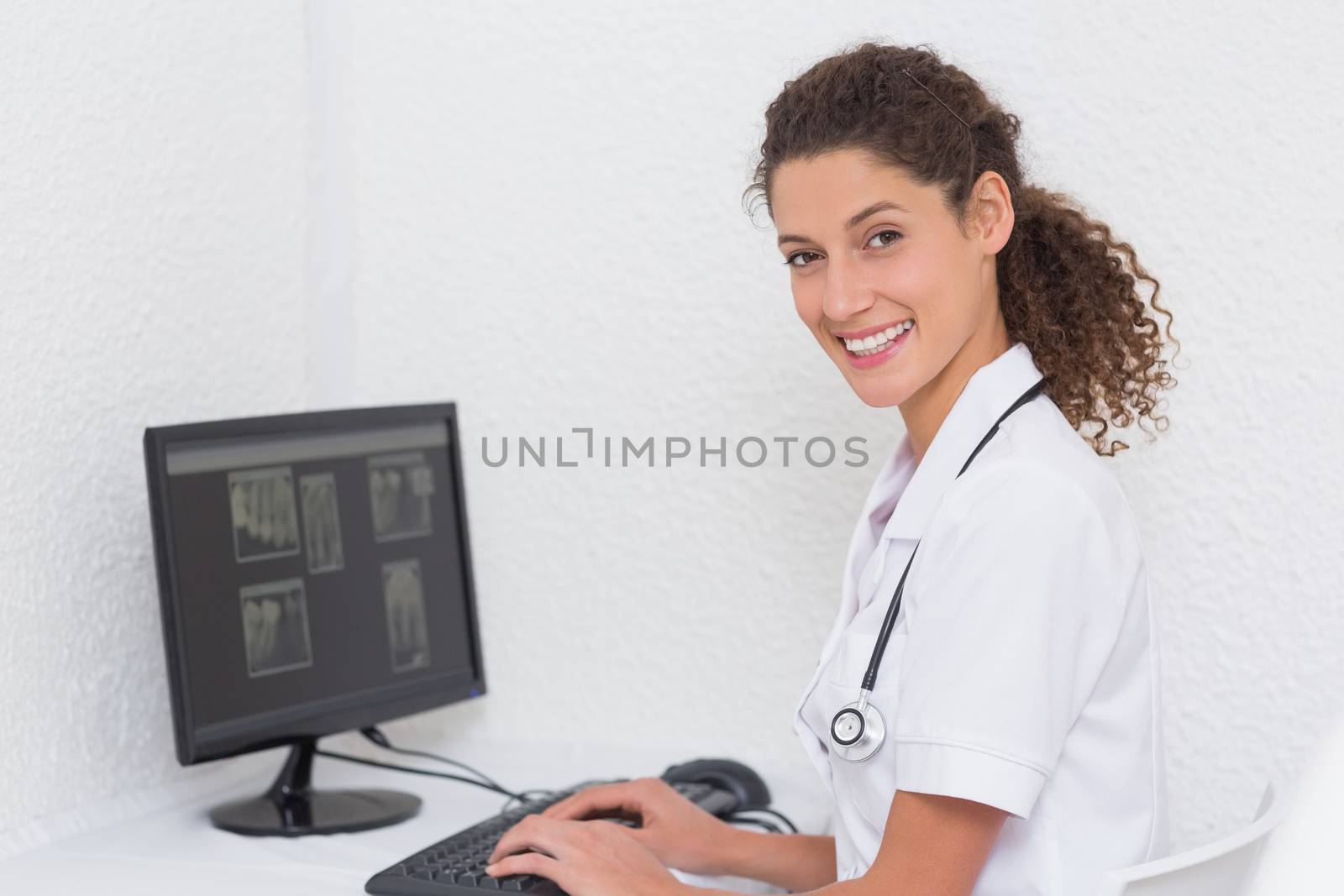 Dental assistant working on computer smiling at camera at the dental clinic