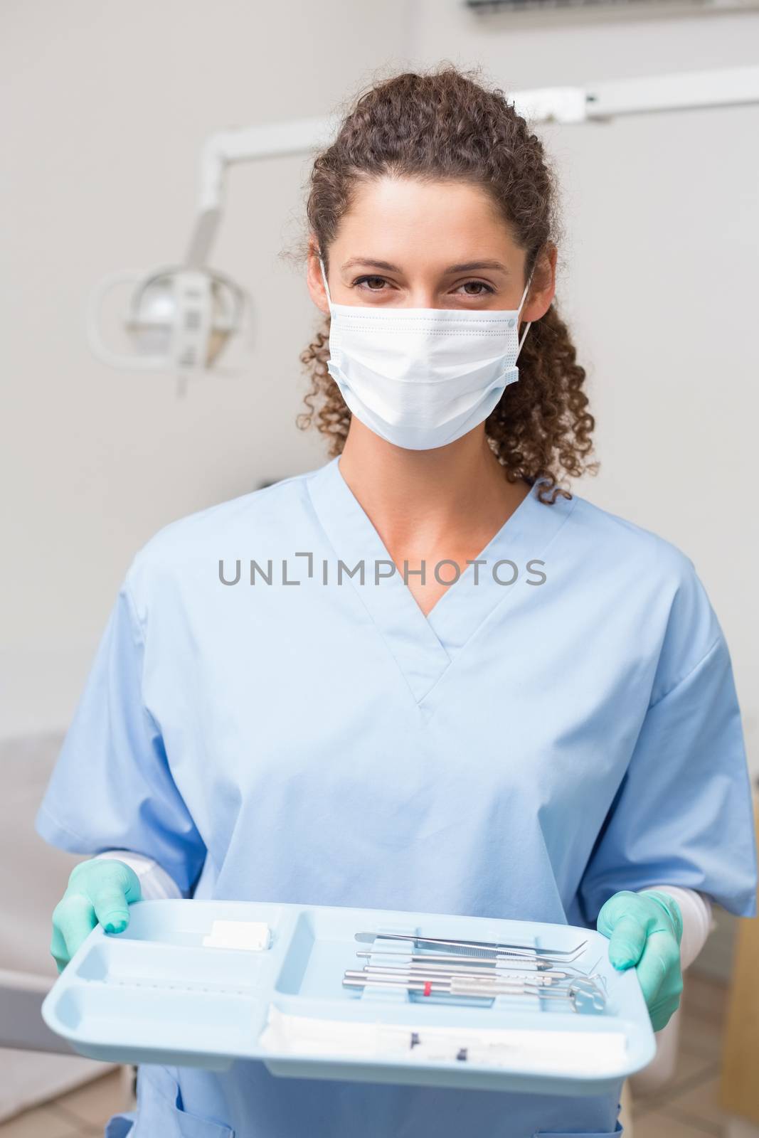 Dentist in blue scrubs holding tray of tools by Wavebreakmedia