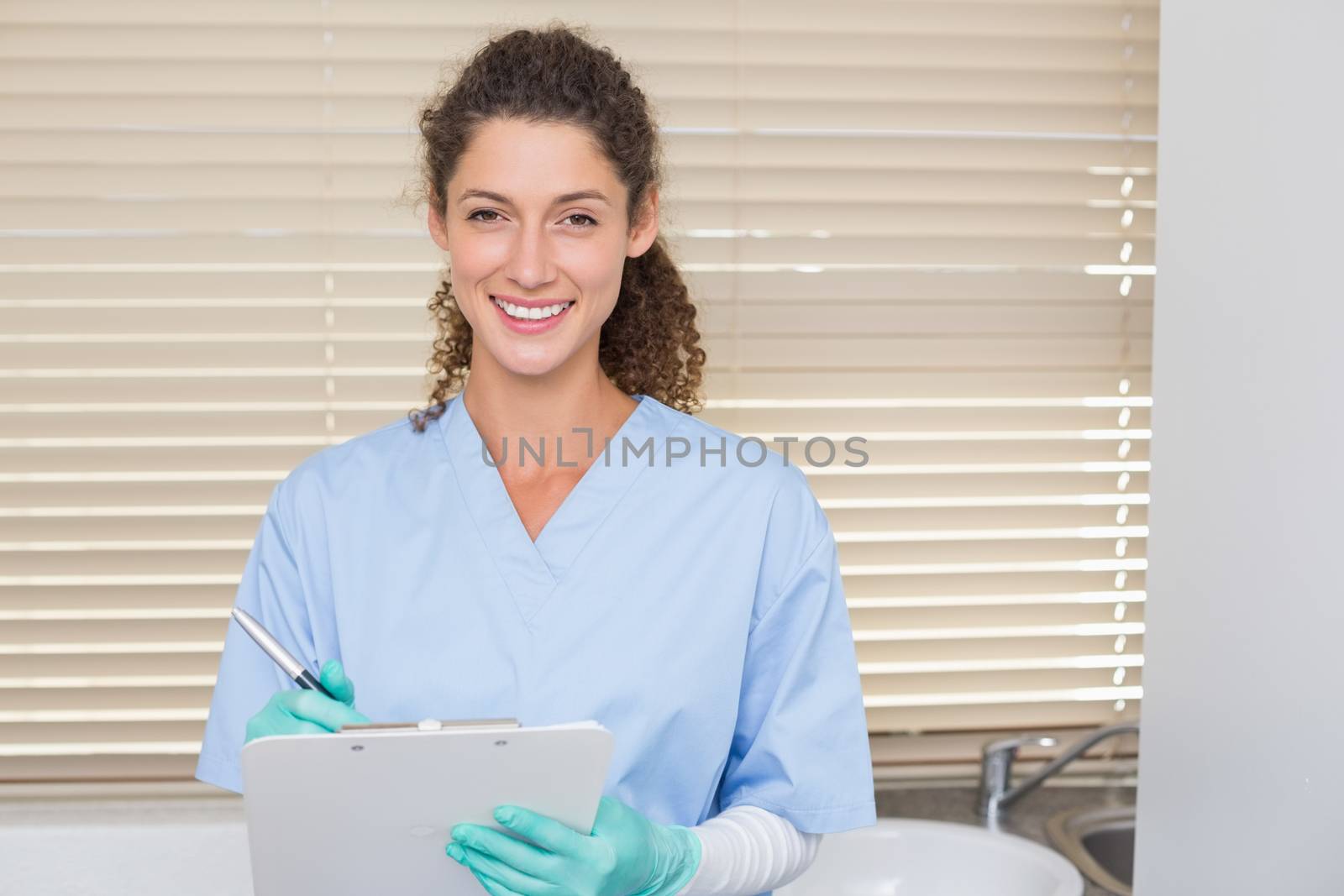 Dentist in blue scrubs writing on clipboard by Wavebreakmedia